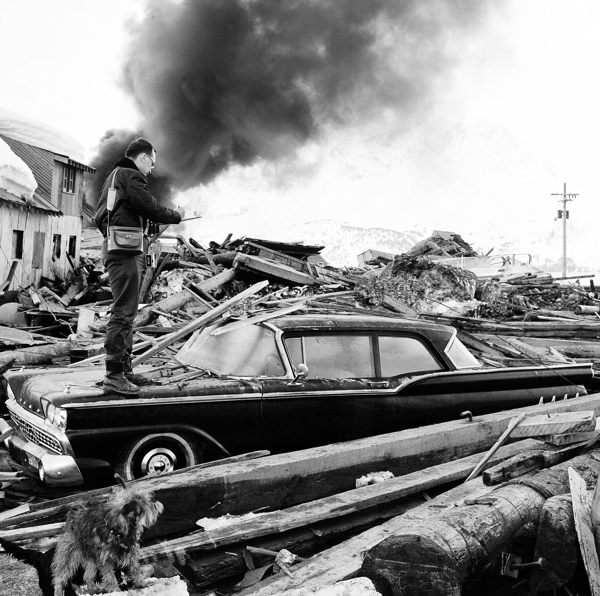 In this March 29, 1964 file photo, a photographer looks over wreckage as smoke rises in the background from burning oil storage tanks at Valdez on March 29, 1964. The city was hit hard by the earthquake that demolished some of Alaska’s most picturesque and largest cities. North America’s largest earthquake rattled Alaska 54 years ago, killing 15 people and creating a tsunami that killed 124 more from Alaska to California. The magnitude 9.2 quake hit at 5:30 p.m. on Good Friday, turning soil beneath parts of Anchorage into jelly and collapsing buildings that were not engineered to withstand the force of colliding continental plates. (Associated Press file)