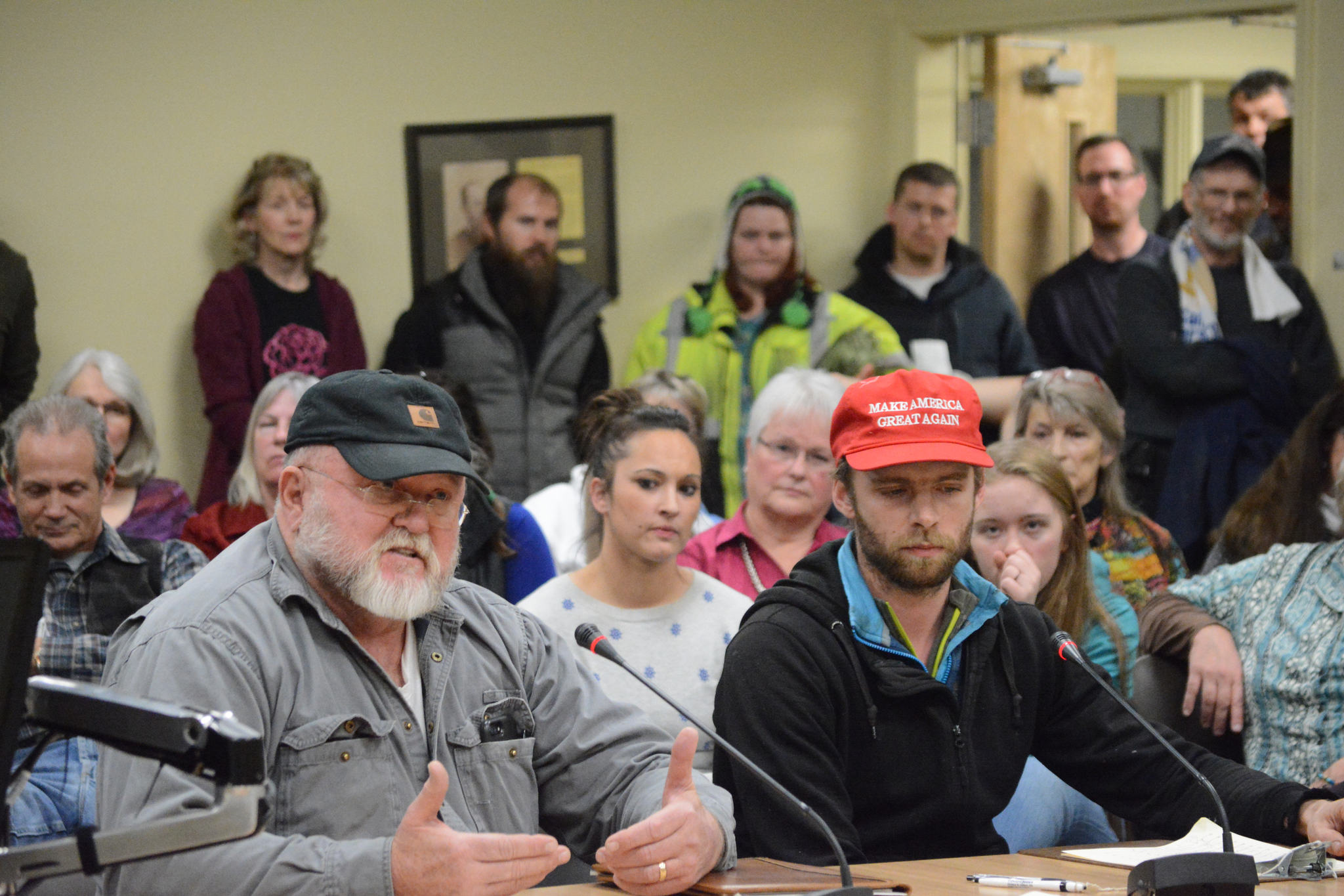 Vernon Atkinson, left, speaks, while Paul Riedel, right, in a “Make America Great Again” hat waits his turn to testify on Resolution 17-019 at the Homer City Council meeting on Monday night.