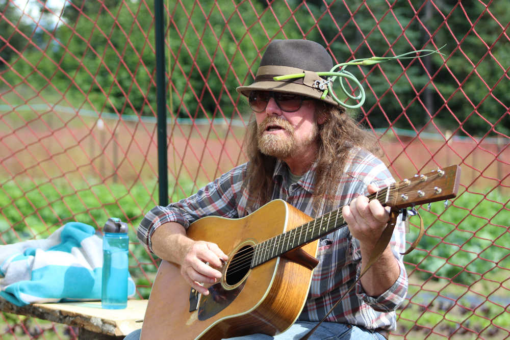 Kenute Tonga strums on his guitar and sings in the sun, adorned with a garlic scape in his hat, during Synergy Gardens' First Annual Great Garlic Scape Festival on Sunday, July 10.