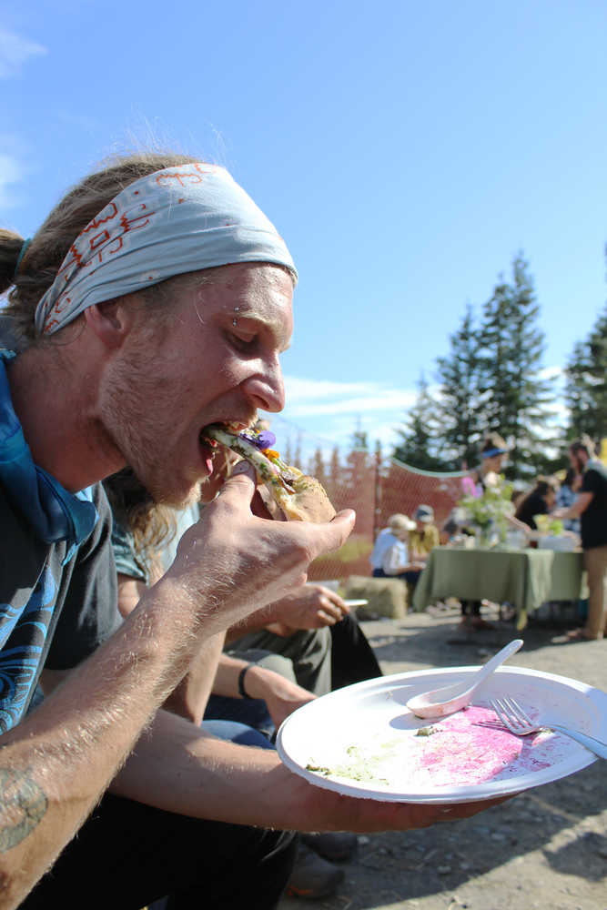 Synergy Gardens volunteer Tyler Schlieman takes a bite of pizza topped with local produce and edible flowers at Synergy Gardens' First Annual Great Garlic Scape Festival.