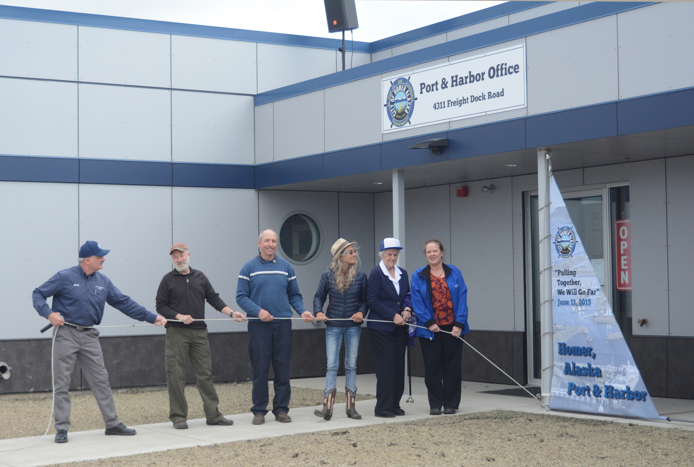 Harbormaster Bryan Hawkins, left, holds down the line after a sail was raised at the ceremonial opening of the new Harbor Office last Thursday. Helping him from left to right are Port and Harbor Commissioner Michael Stockburger, Homer City council member Bryan Zak, Port and Harbor Commissioner Catherine Ulmer, former council member Barbara Howard and Homer Mayor Beth Wythe. Hawkins said he chose raising a sail instead of a ribbon cutting in keeping with the harbor theme.-Photo by Michael Armstrong, Homer News