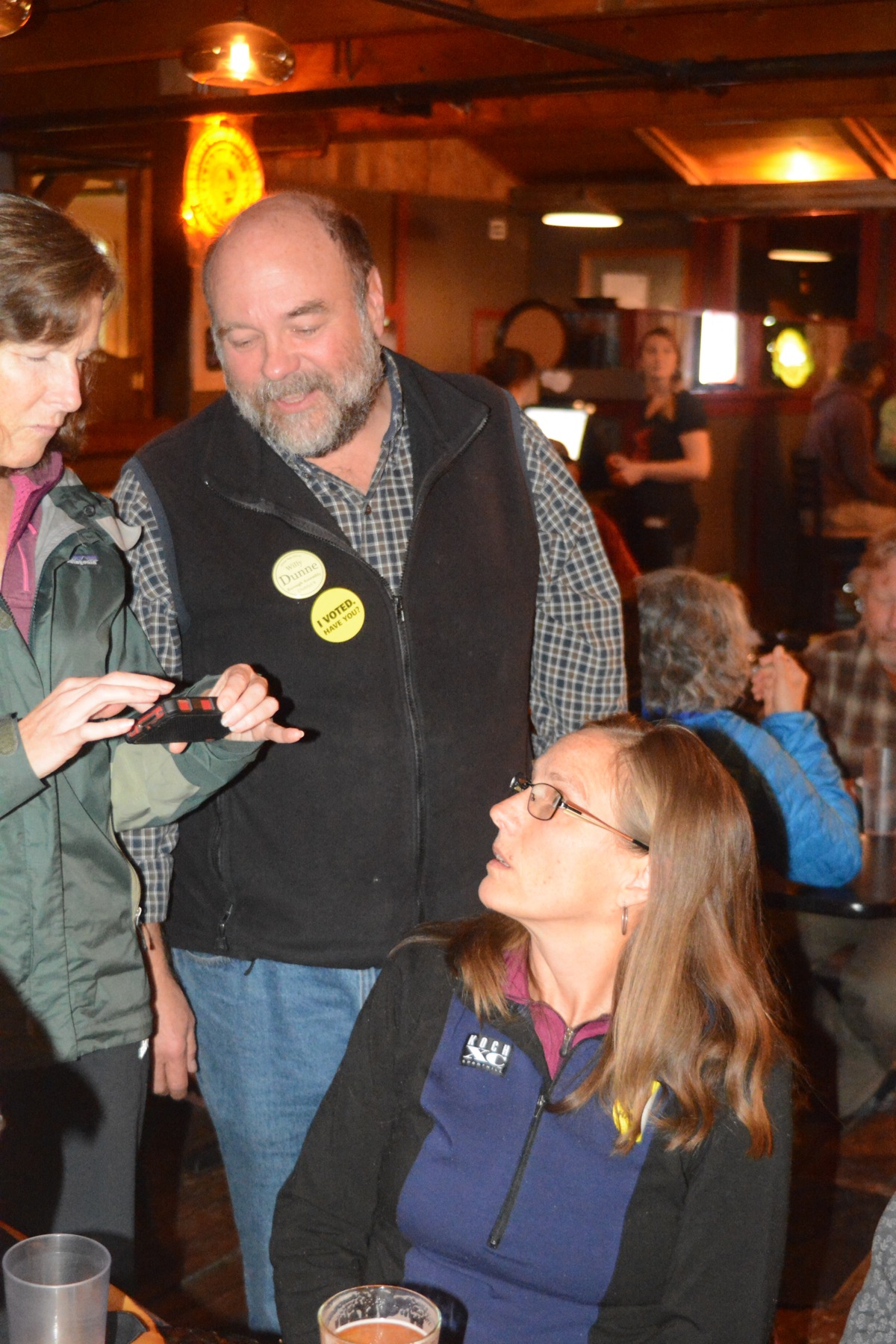 Sue Mauger, left, shows Willy Dunne, center, and Donna Aderhold election results on her smart phone at an election party Tuesday night at Alice's Champagne Palace. Dunne is the apparent winner in the race for Kenai Peninsula Borough Assembly while Aderhold took first place in the two-seat Homer City Council election.-Photo by Michael Armstrong, Homer News