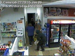 This screen capture of video footage taken at the Short Stop Tesoro gas station hows a man in a hoody standing behind two people in the store. The man holds a bag containing cash and cigarettes.-Photo provided, Homer Police Department