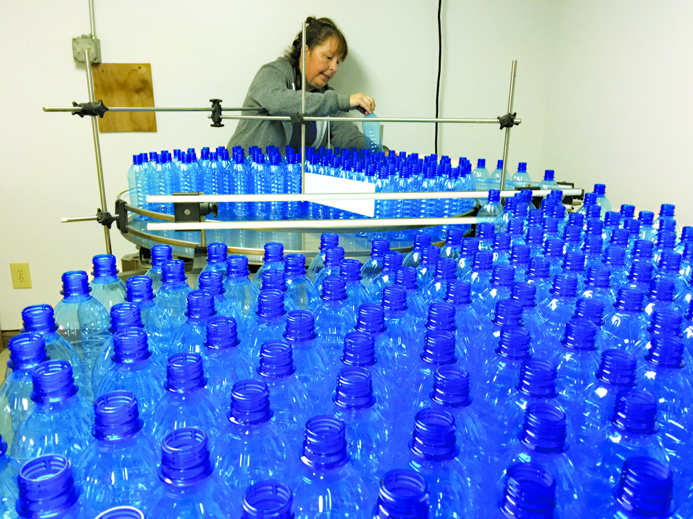 Liz Doan gets bottles ready to head down a conveyor belt where they will be filled with water, capped and labeled.-Photo by Lori Evans, Homer News