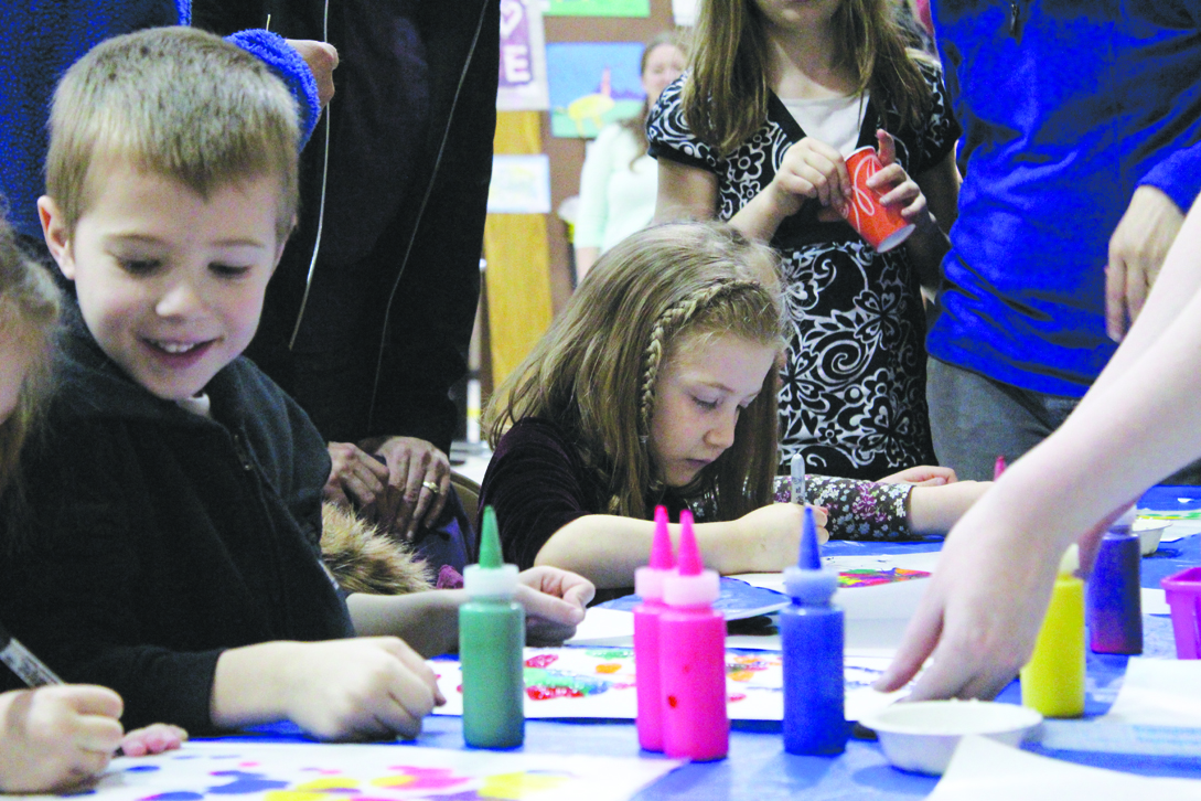 Finn Zeiset looks over at his neighbor’s project, while Kimberly Socha works dilligently on her work of art at the Paul Banks Elementary First Friday Art Extravaganza. A long table at the event provided space for kids to paint and color.