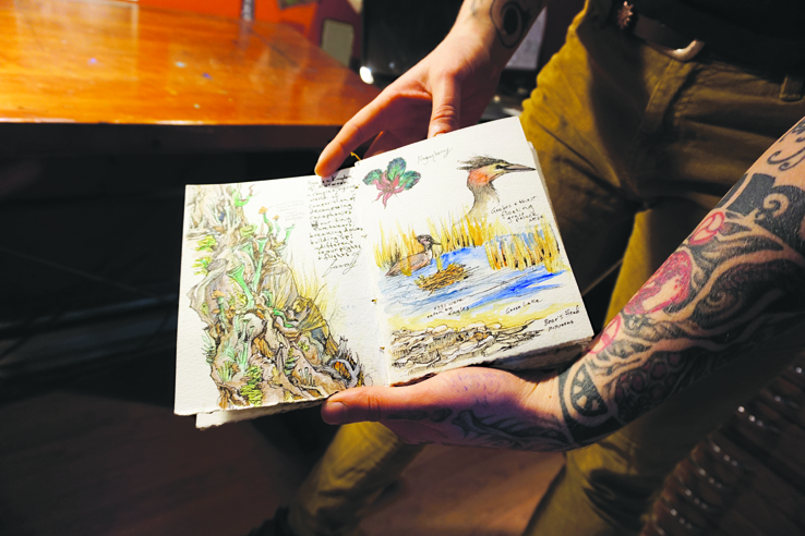 Sarah shows some pages from a journal project she’s working on. A tattoo artist, she did the ink on her left arm.-Photo by Michael Armstrong, Homer News