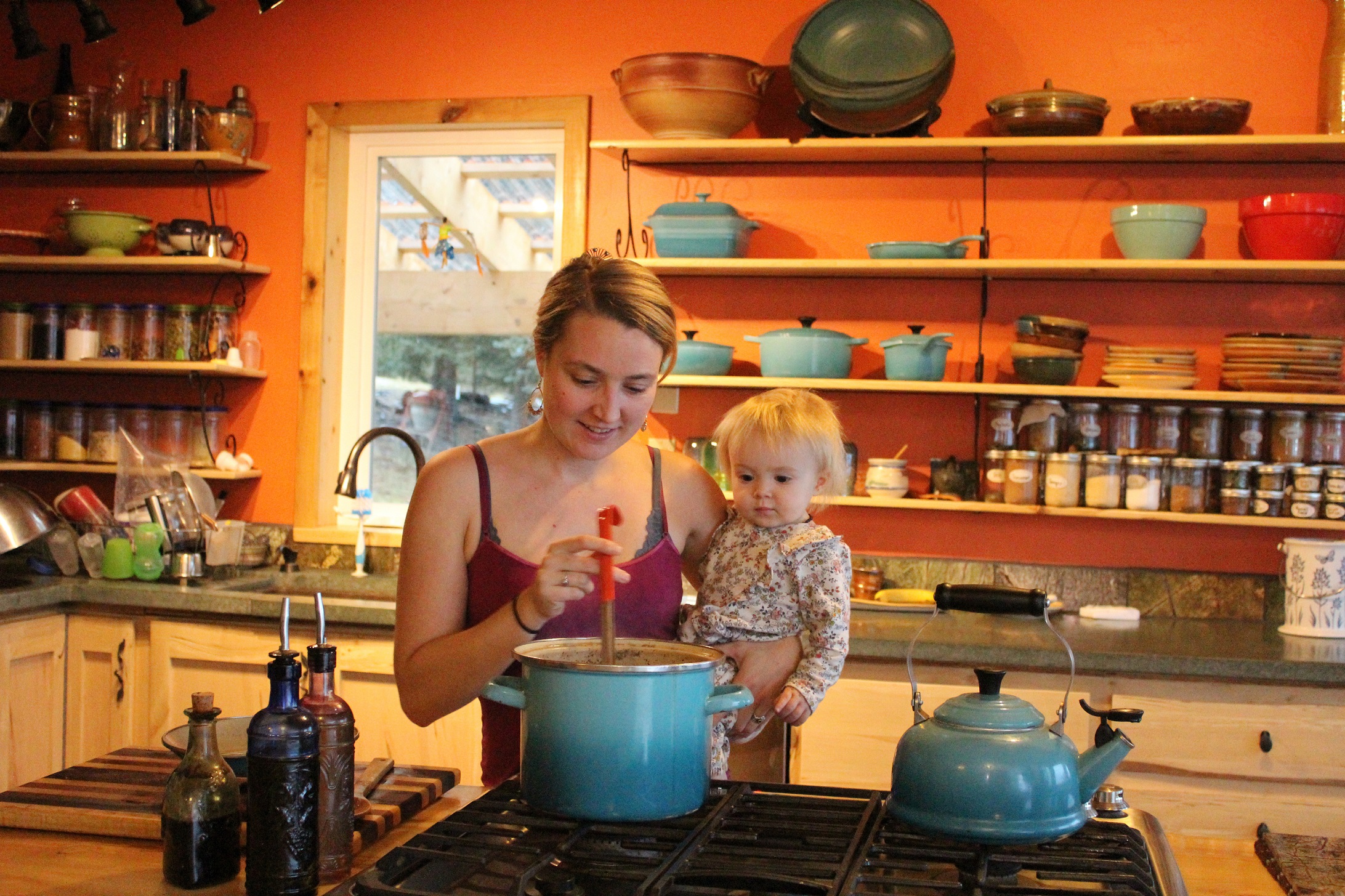 Eve Kilcher stirs a pot of chicken soup while holding Sparrow. The Kilcher's kitchen, which is the backdrop of the cover photo on Homestead Kitchen, was under construction for the majority of the time the Kilchers worked on the cookbook.-Photo by Anna Frost, Homer News