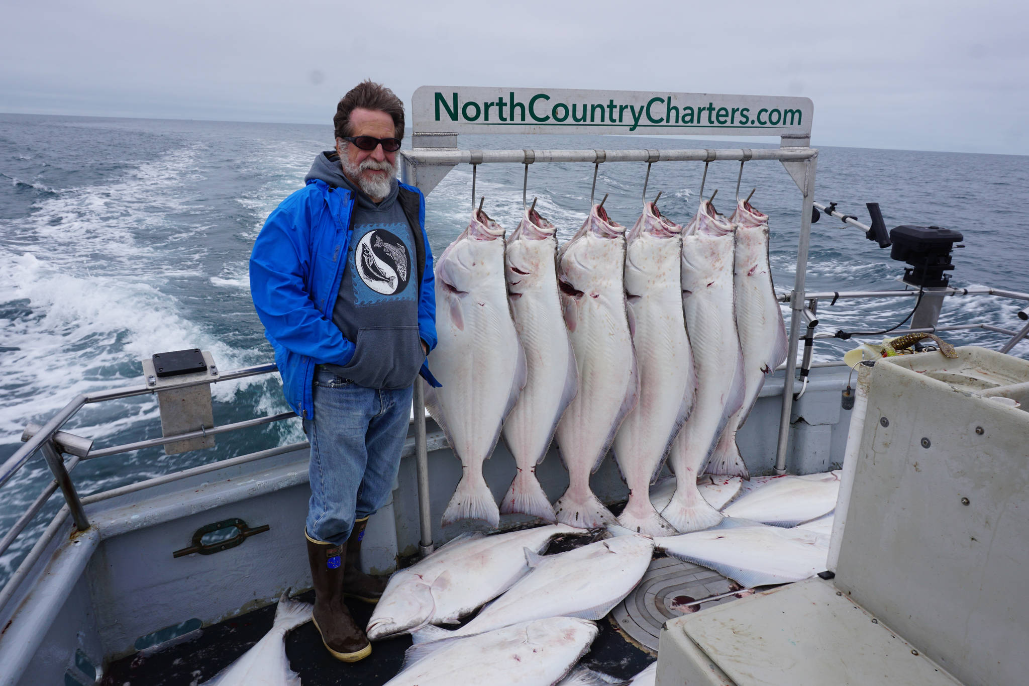 Michael Armstrong stands by a rack of halibut on the Irish as the North Country Charters boat returns to Homer, Alaska. He caught two of the smaller fish on the deck. The 16 fishermen on the 53-foot boat all limited out on a July 16, 2017 guided halibut fishing trip. Photo by Øisten Stokke Berget