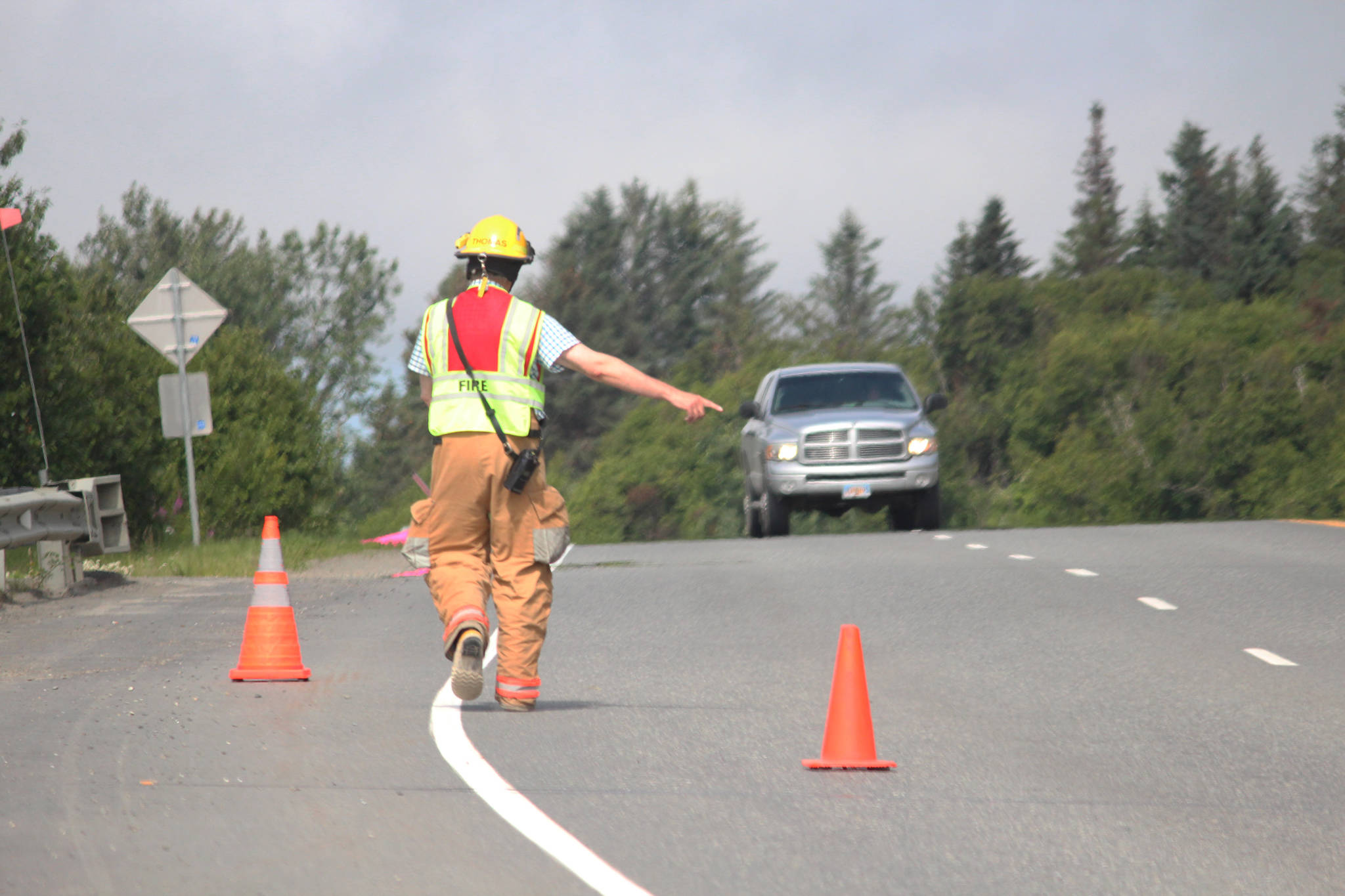 A first responder directs an oncoming truck around the cones set out to give crews space while they responded to a report of a truck that had fallen over the edge near Baycrest Overlook on Monday, July 24, 2017 in Homer, Alaska. First responders found the pickup truck that had fallen over the edge after hitting a guardrail, and searched for a possible victim until getting a report that the driver had crashed several days earlier and had walked away uninjured. Photo by Megan Pacer/Homer News