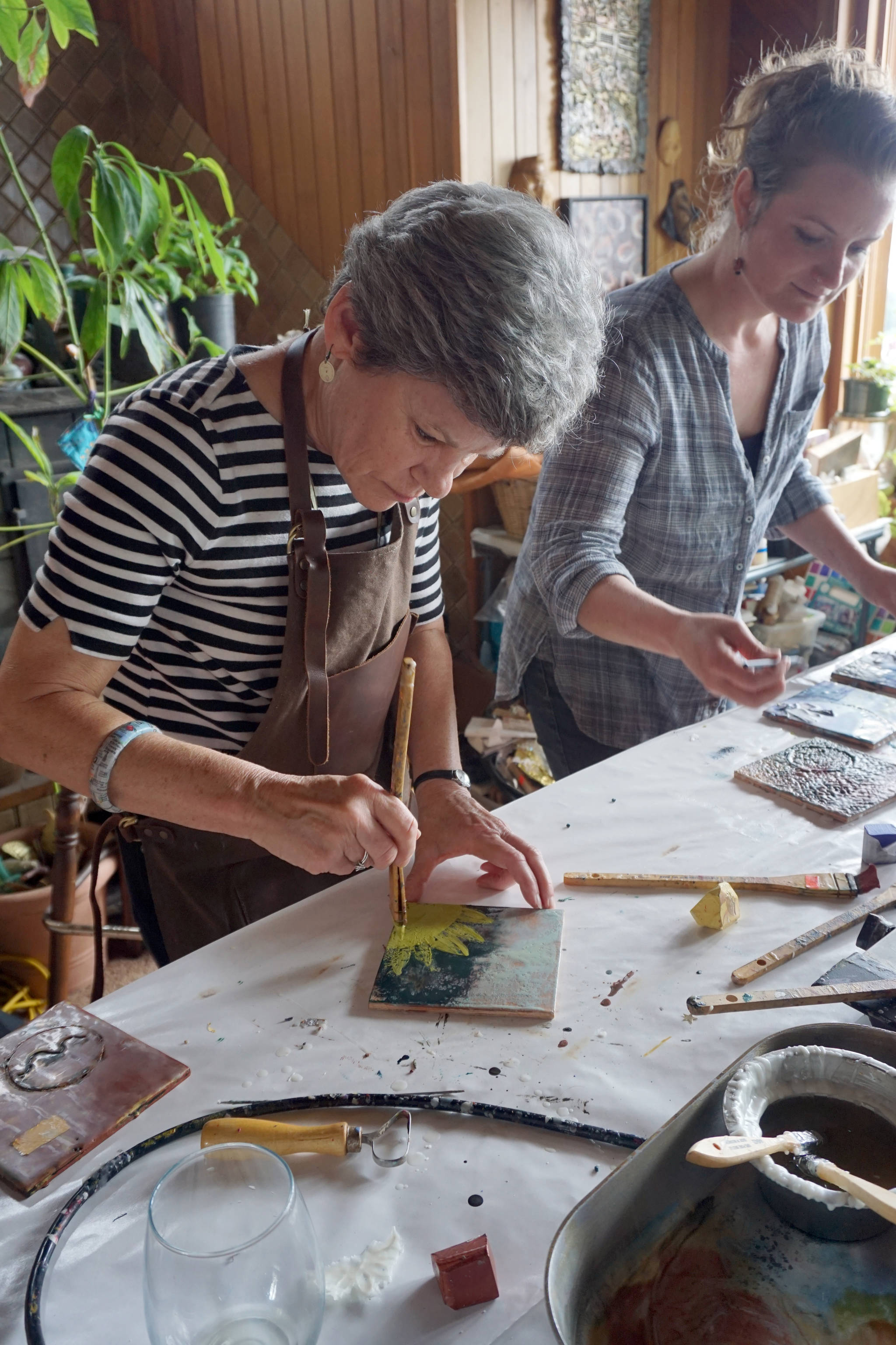 Jane Bernard of Morgan City, La., left, and Becca Bottebaum paint with encaustics in Ann-Margret Wimmerstedts Wax. Wine & Wimmerstedt class held July 30, 2017 at Wimmerstedt’s home. (Photo by Michael Armstrong/Homer News)