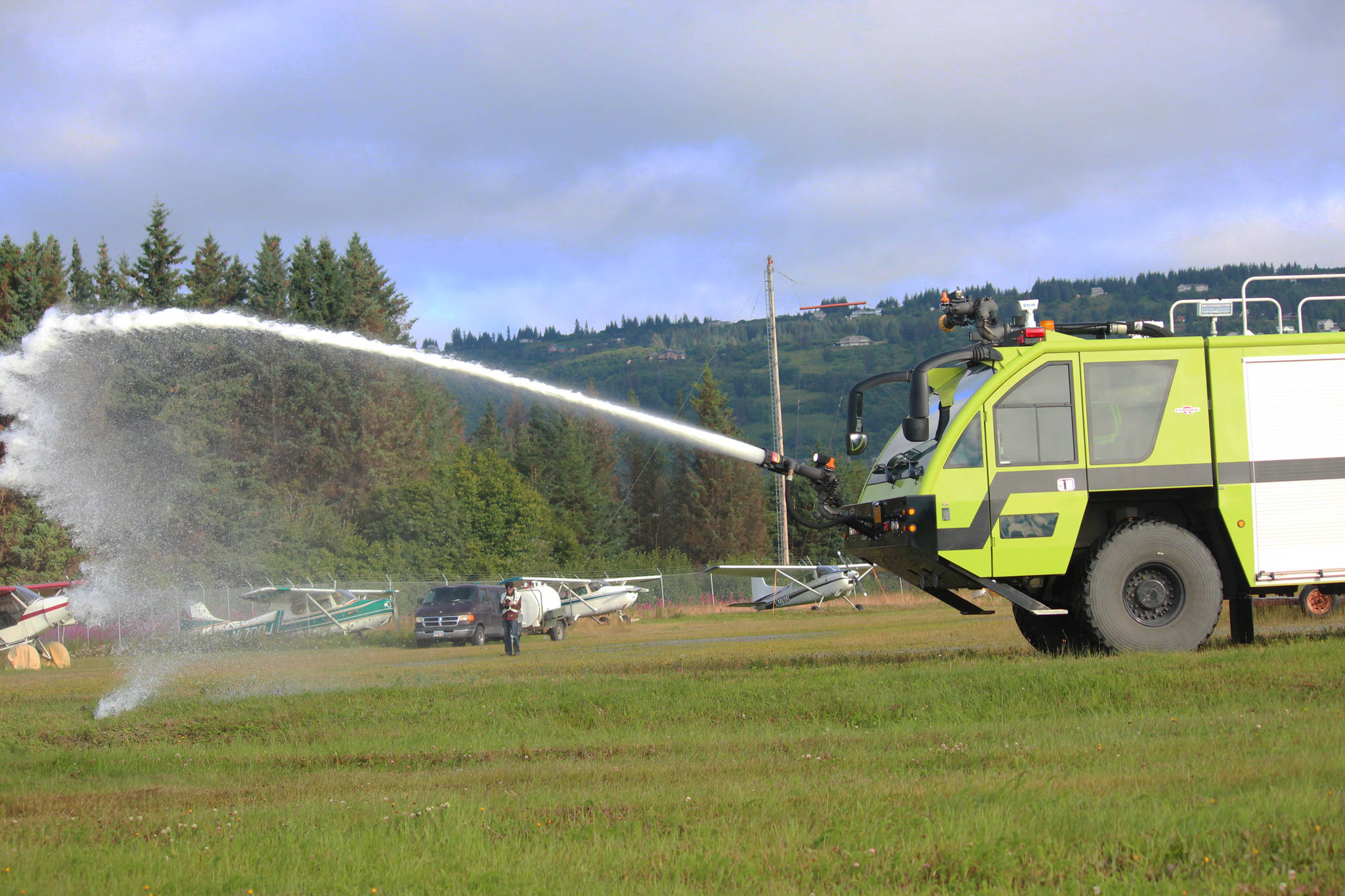 Foam sprays out from a fire engine and onto a bus used as a crash plane and filled with volunteer “victims” during a simulated airplane crash Saturday, Aug. 19, 2017 at the Homer Airport in Homer, Alaska. The emergency drill happens every three years and is required for the airport to stay in Federal Aviation Administration compliance. It tests the ability of airport personnel and members of area emergency response agencies to handle various disaster scenarios at the airport, like a crash. (Photo by Megan Pacer/Homer News)