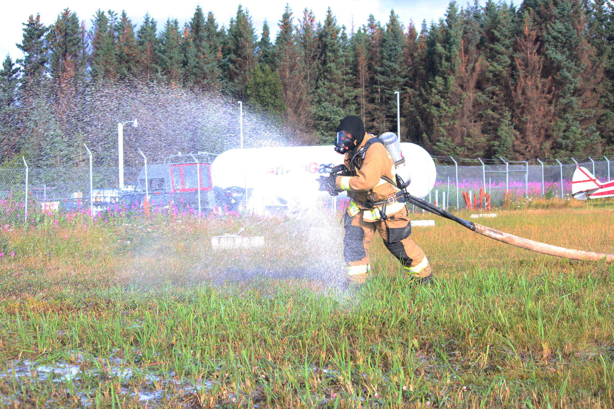 Firefighter Jesse Sherwood sprays foam at a bus being used for a simulated airplane crash Saturday, Aug. 19. 2017 at the Homer Airport in Homer, Alaska. The simulation was part of an emergency drill done at the airport every three years to test the ability of emergency response agencies and airport personnel to handle various scenarios there. (Photo by Megan Pacer/Homer News)