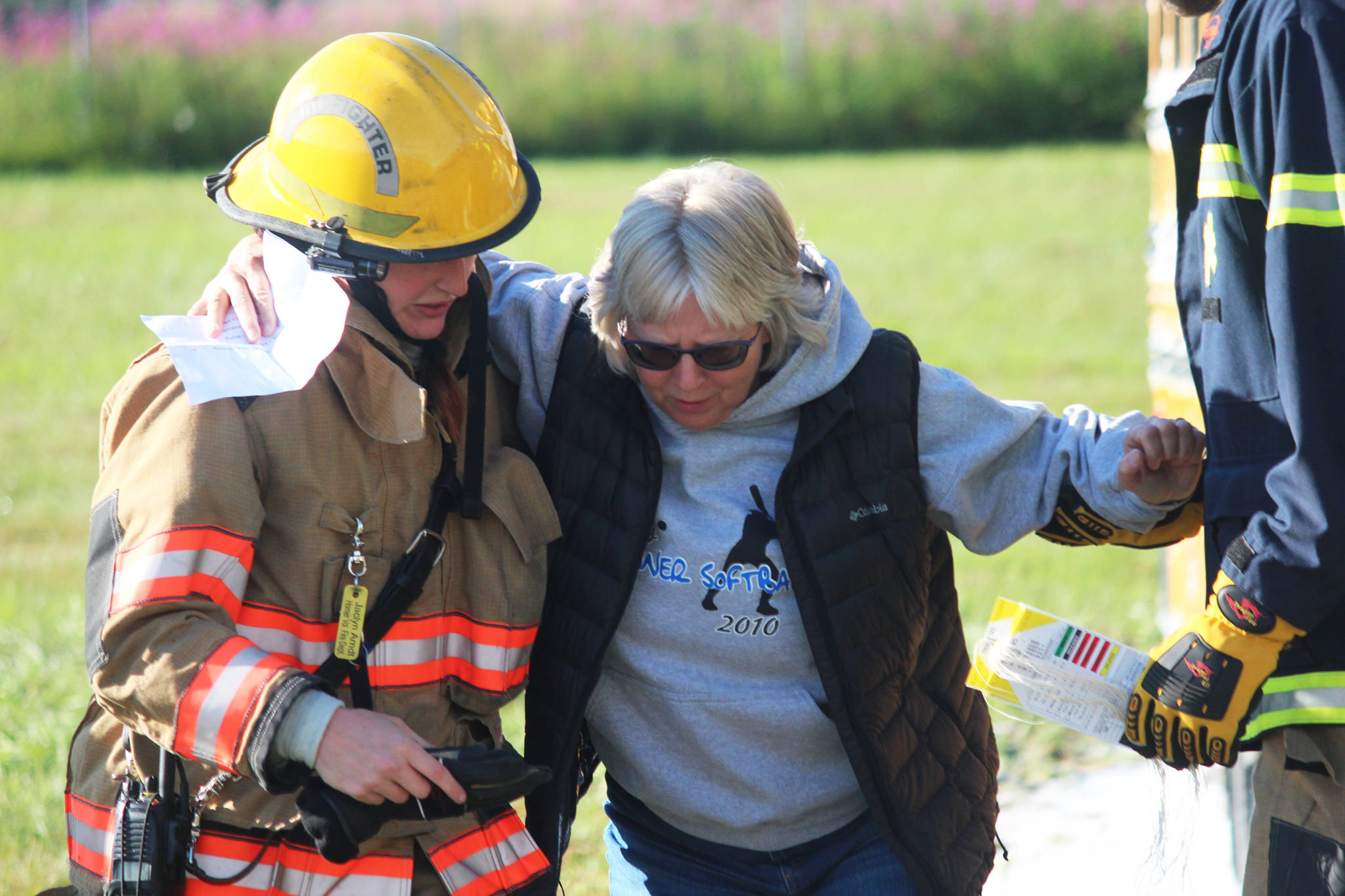 Homer City Council member Shelly Erickson feigns injury as she is escorted from a bus during a simulated airplane crash Saturday, Aug. 19, 2017 at the Homer Airport in Homer, Alaska. The emergency drill is held every three years and is required for the airport to remain in Federal Aviation Administration compliance. Erickson was one of more than 20 volunteers who posed as crash victims. (Photo by Megan Pacer/Homer News)