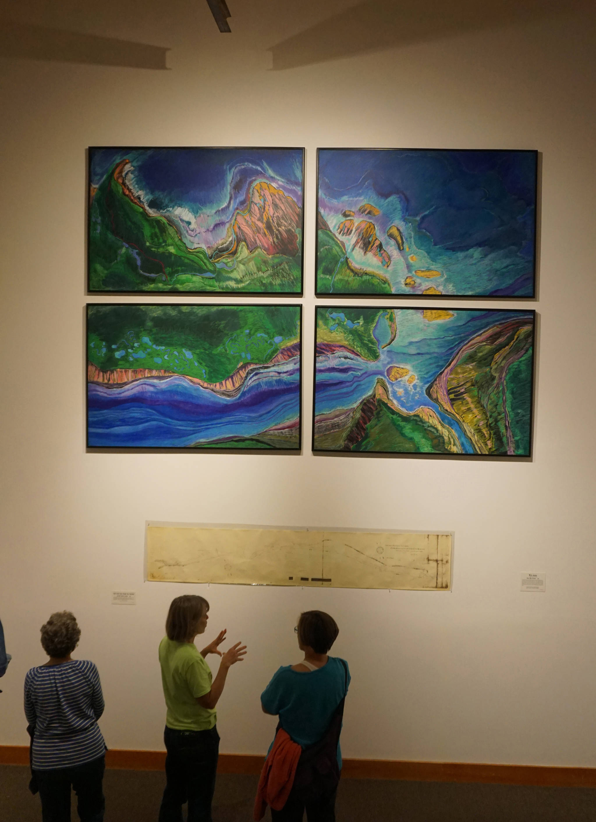 Visitors to the Pratt Museum look at “Wild Alaska,” above, by Karla Moss Freeman, and a 1900 map of the Cook Inlet Coal Fields railroad, one of the historic pieces included in cARTography exhibit Tuesday, Aug. 22, 2017 at the Pratt Museum, Homer, Alaska. (Photo by Michael Armstrong, Homer News)