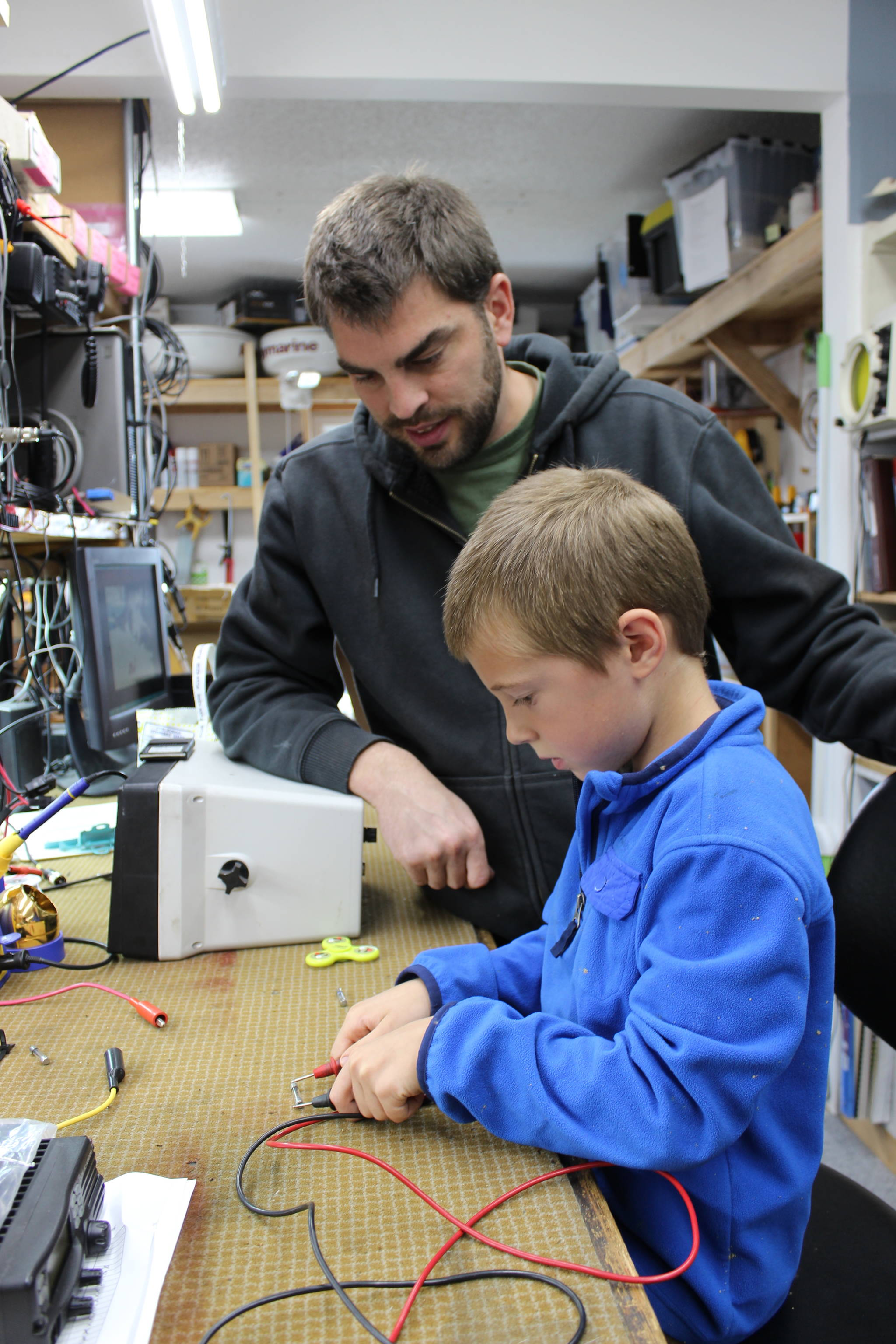 In a good example of building the next generation of marine trades-related professionals, Mark Zeiset, owner of South Central Radar, teaches his son Finn, 6, how to test fuses. )Photo by McKibben Jackinsky for the Homer News)