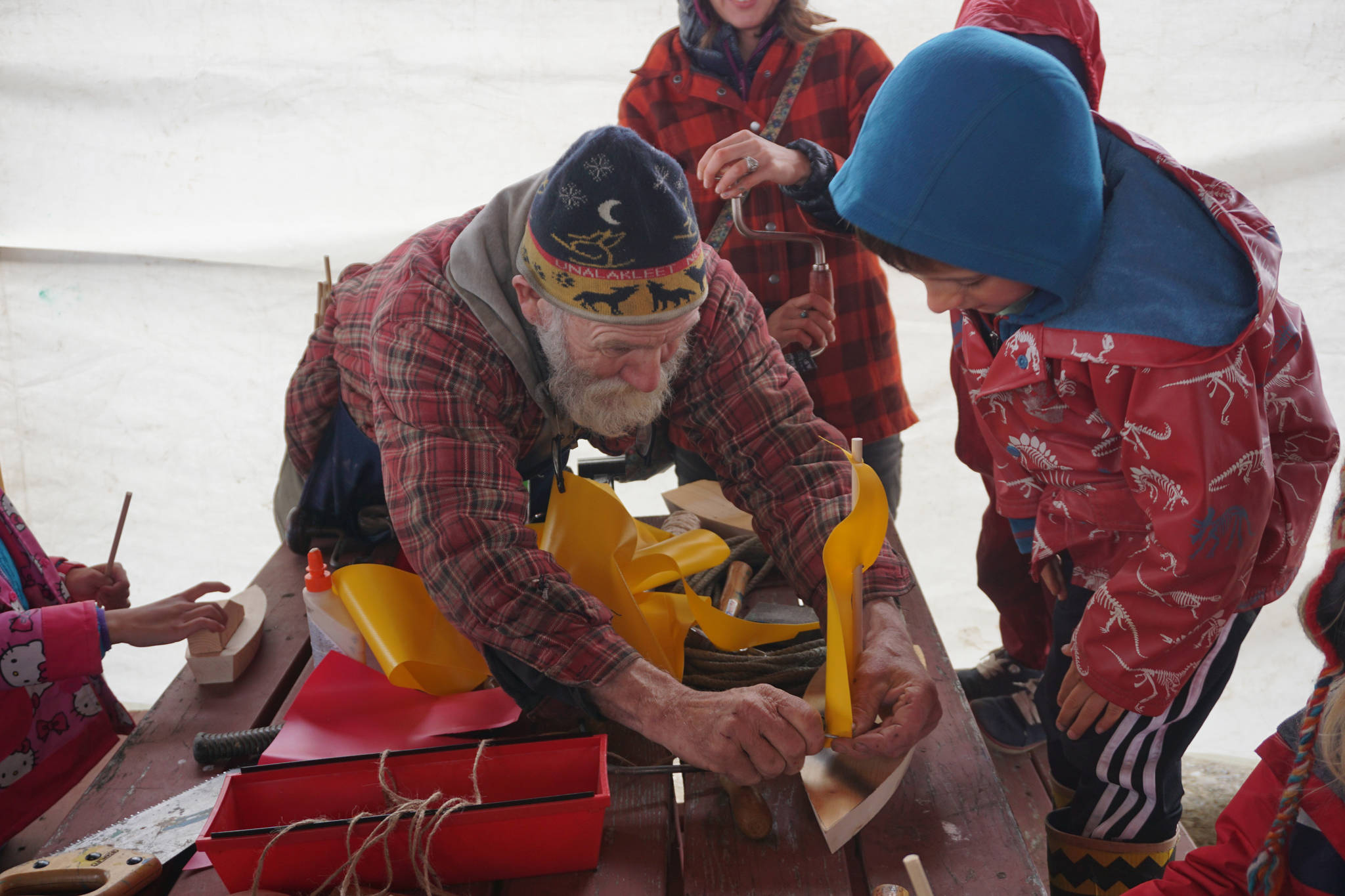 John Miles, left, helps Ike Mitchell work on a boat during the Kachemak Bay Wooden Boat Society Festival on Saturday, Sept. 2, 2017 at the Nick Dudiak Fishing Lagoon campground in Homer, Alaska. Ike’s mother, Jamey Cloud, and his brother, Charlie Mitchell, watch. (Photo by Michael Armstrong, Homer News)