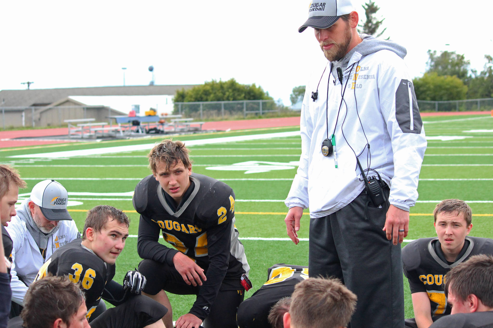 Head Coach Justin Zank counsels the Cougar football team, including junior Kalinik Reutov, left, sophomore Zasima Martushev, center and junior Nikola Reutov, after their 18-40 loss to Nikiski High School on Saturday, Sept. 2, 2017 in Homer, Alaska. With 14 players at the game, Zank said he had the largest group that’s been assembled so far this season. (Photo by Megan Pacer/Homer News)