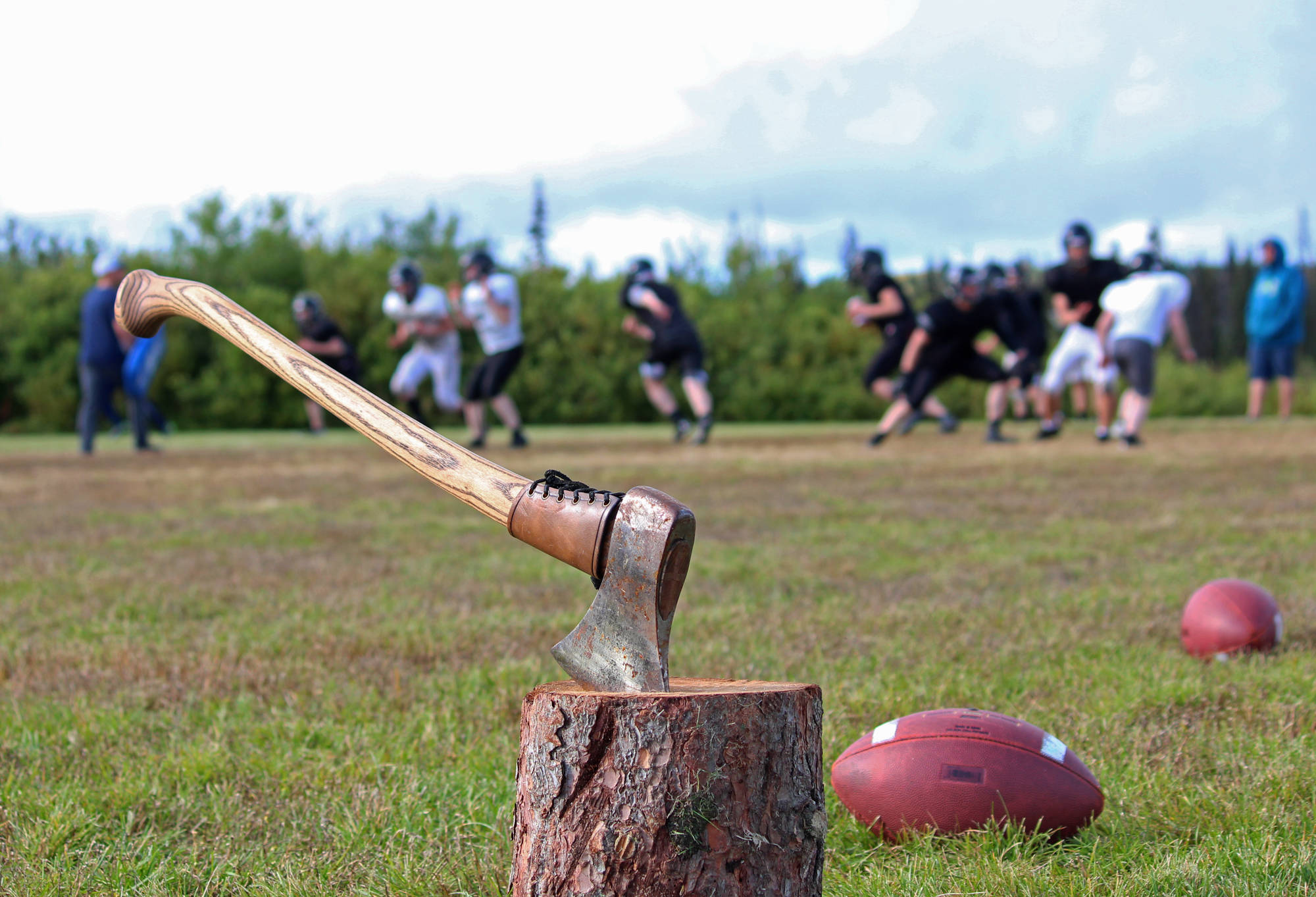 Members of the Cougars football team, made up of players from three Russian Old Believer schools, practice in a field Friday, Sept. 1, 2017 in a field behind McNeil Canyon Elementary in Fritz Creek, Alaska. The axe stuck in the stump in the foreground is a new tradition started this year by Head Coach Justin Zank. He tells his players to “be the axe.” (Photo by Megan Pacer/Homer News)