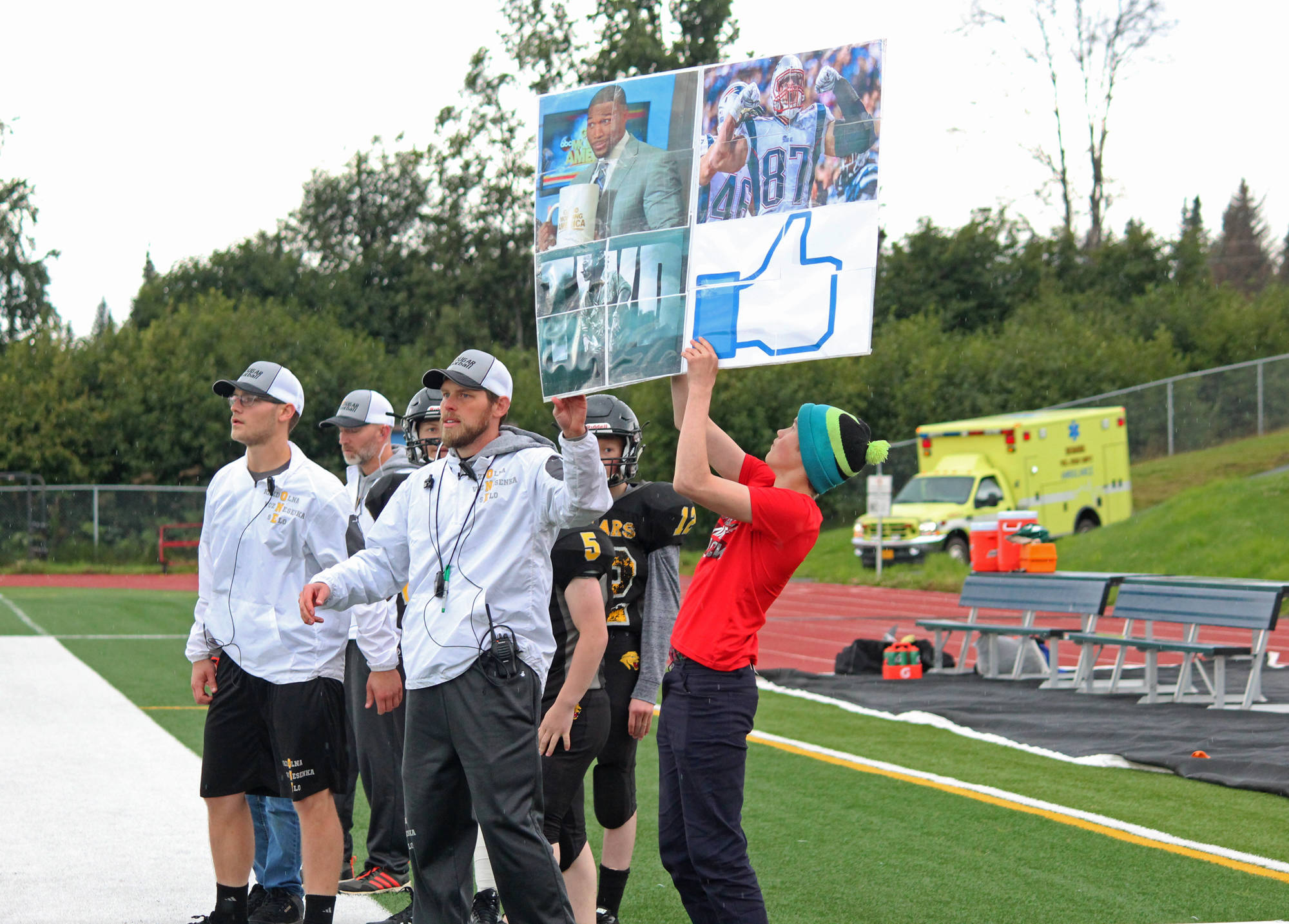 Cougars Head Coach Justin Zank helps hold up a sign to communicate plays to his team during their game against Nikiski High School on Saturday, Sept. 2, 2017 in Homer, Alaska. Zank uses pictures to represent the names of plays. One sign Saturday contained a play written in Cyrillic. (Photo by Megan Pacer/Homer News)