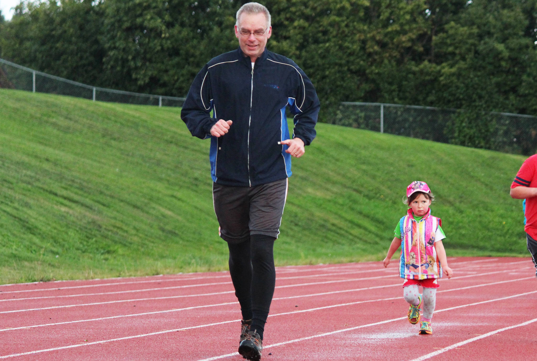 Robert Green runs with his daughter, 4-year-old Miranda Green, during the Mariner Mile fundraising event Thursday, Sept. 14, 2017 at the Homer High School track in Homer, Alaska. Participants signed up to run one mile around the track in different heats, with proceeds going to the Kachemak Bay Running Club. (Photo by Megan Pacer/Homer News)