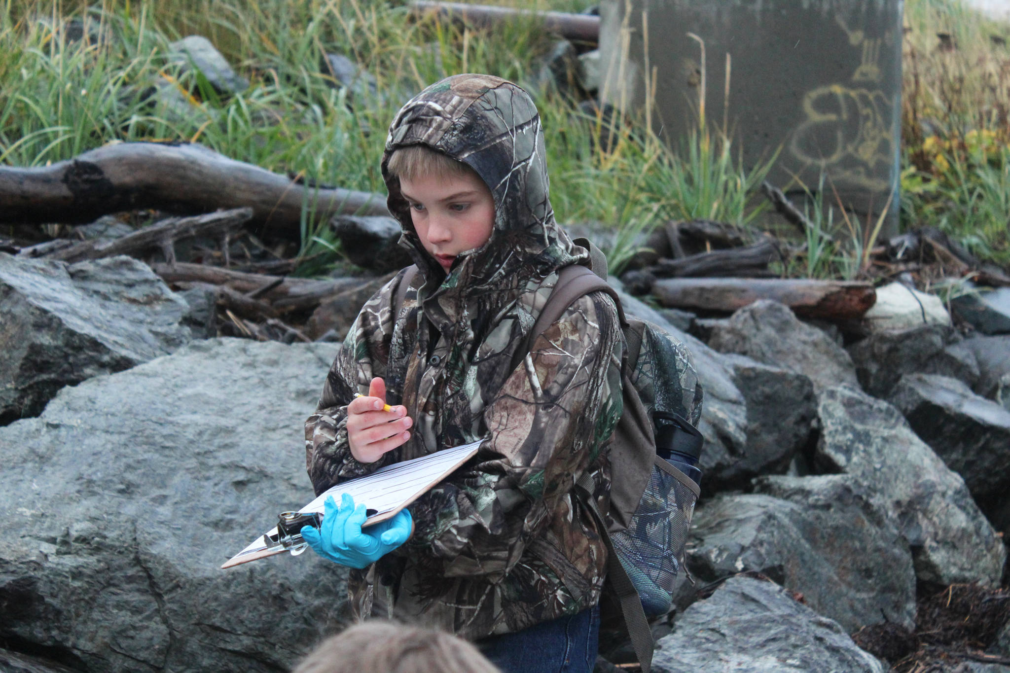 Tanner Johnson, a fourth grader at McNeil Canyon Elementary School, marks down his group’s findings on a clipboard while he and classmates clean the shoreline on Friday, Sept. 22, 2017 near Mariner Park in Homer, Alaska. Many school classes and citizen groups sign up each year to scour a section of coast during the annual Kachemak Bay CoastWalk, hosted by the Center for Alaskan Coastal Studies. (Photo by Megan Pacer/Homer News)