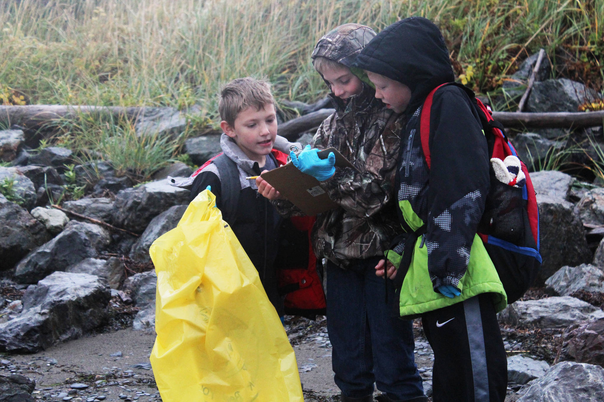 Niko Erickson (left), Tanner Johnson (center) and Zephaniah Weisser (right) look at the progress they’ve made in recording their findings on the shoreline of Kachemak Bay on Friday, Sept. 22, 2017 near Mariner Park in Homer, Alaska. Several classes from McNeil Canyon Elementary School participated in this year’s Kachemak Bay CoastWalk, in which students and citizen groups can adopt a section of coast to clean up. (Photo by Megan Pacer/Homer News)