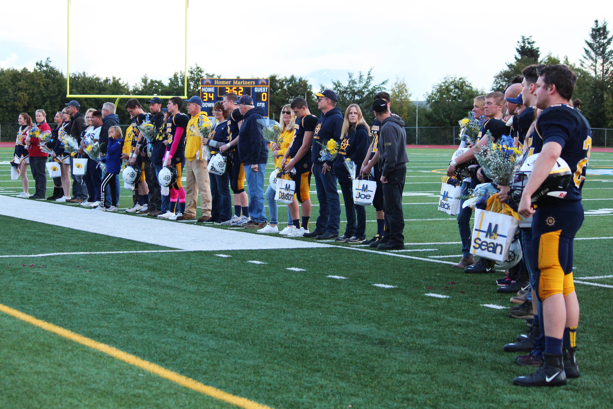 Seniors football players and cheerleaders from Homer High School stand on the field with their family members to be recognized during a senior night presentation during halftime of the game between the Mariners and the Head of the Bay Cougars on Friday, Sept. 29, 2017 at the Mariner field in Homer, Alaska. (Photo by Megan Pacer/Homer News)