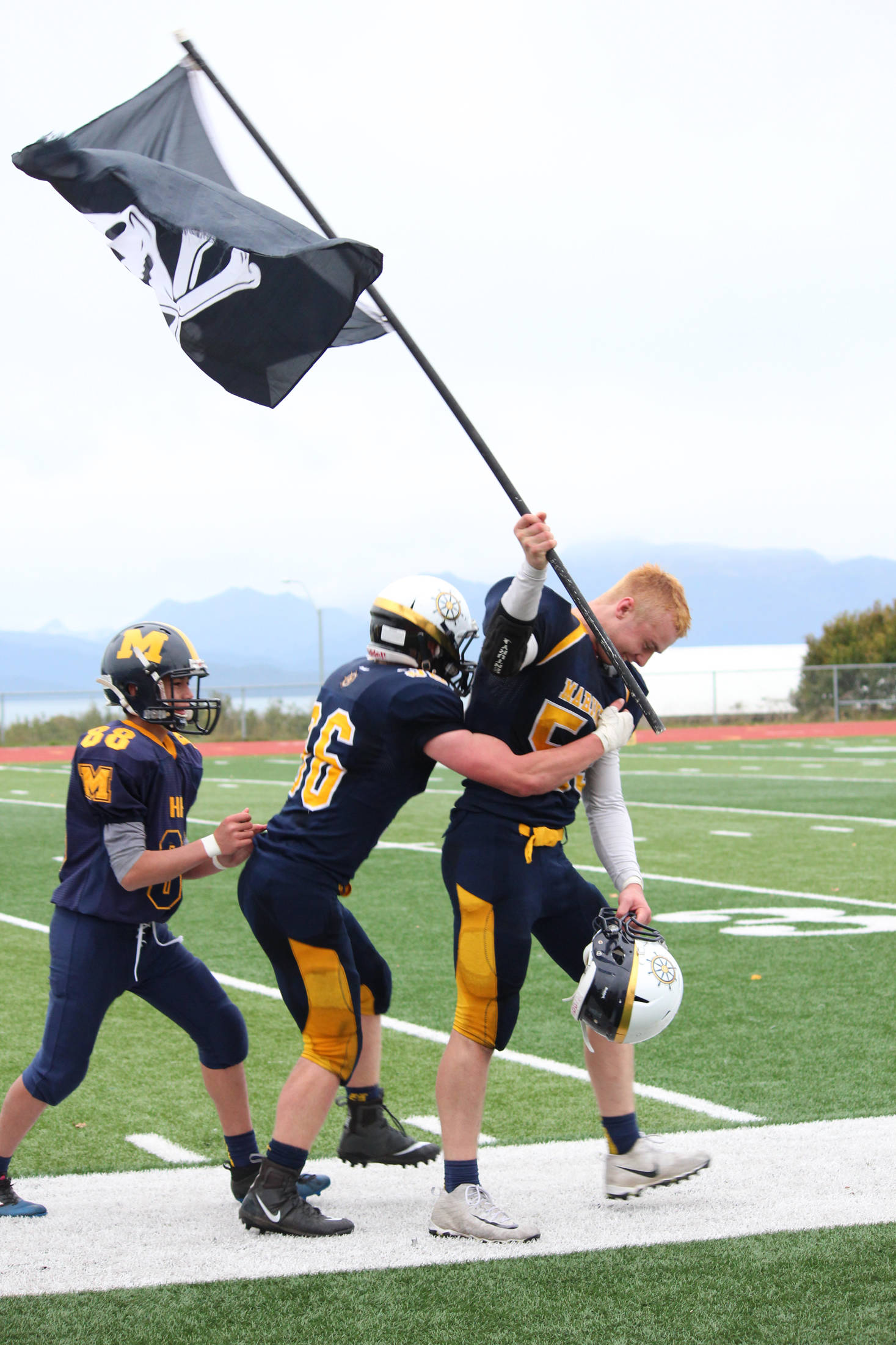 Senior Levi Smith gets a hug from a teammate as he walks of the field at Homer High School carrying a pirate flag Saturday, Oct. 7, 2017 following the varsity football team’s win over Ben Eielson High School 33-21 in Homer, Alaska. The Mariners now head to the ASAA First National Bowl Series Division III Championship. (Photo by Megan Pacer/Homer News)