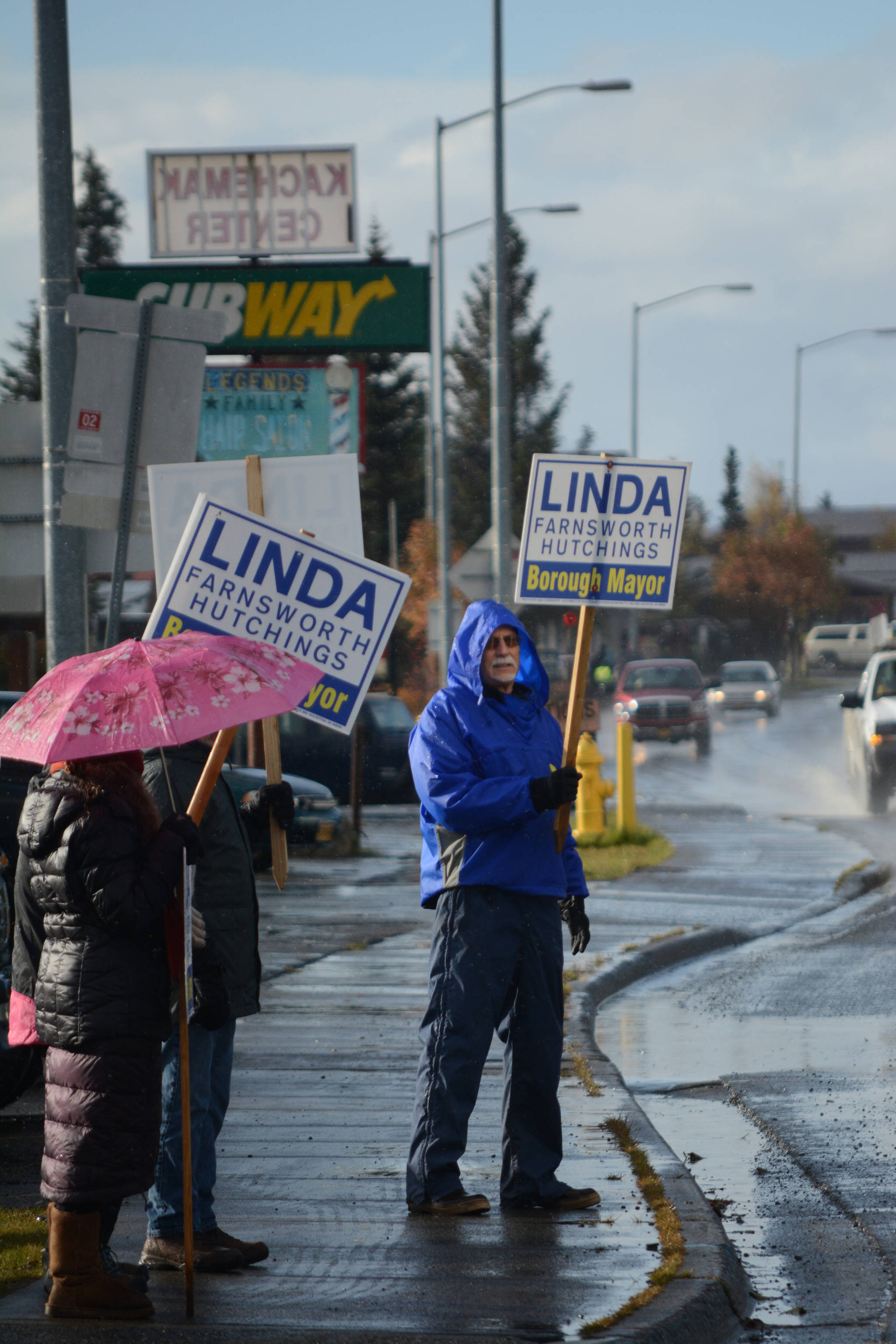 Wayne Aderhold, front, waves signs for Linda Hutchings on Tuesday afternoon, Oct. 24, 2017, in Homer, Alaska, on Pioneer Avenue. To his left are Marjorie Ringer, with umbrella, and Ron Keffer. (Photo by Michael Armstrong, Homer News)