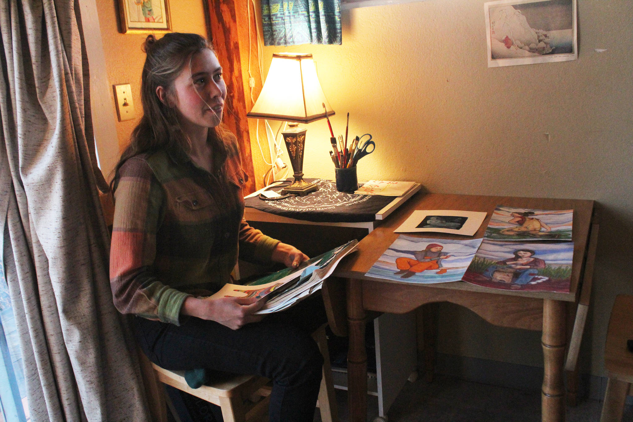 Oceana Wills, a local artist and commercial fisherman, goes through some of her paintings Friday, Nov. 10, 2017 at the cabin where she’s living for the winter in Kachemak City, Alaska. (Photo by Megan Pacer/Homer News)