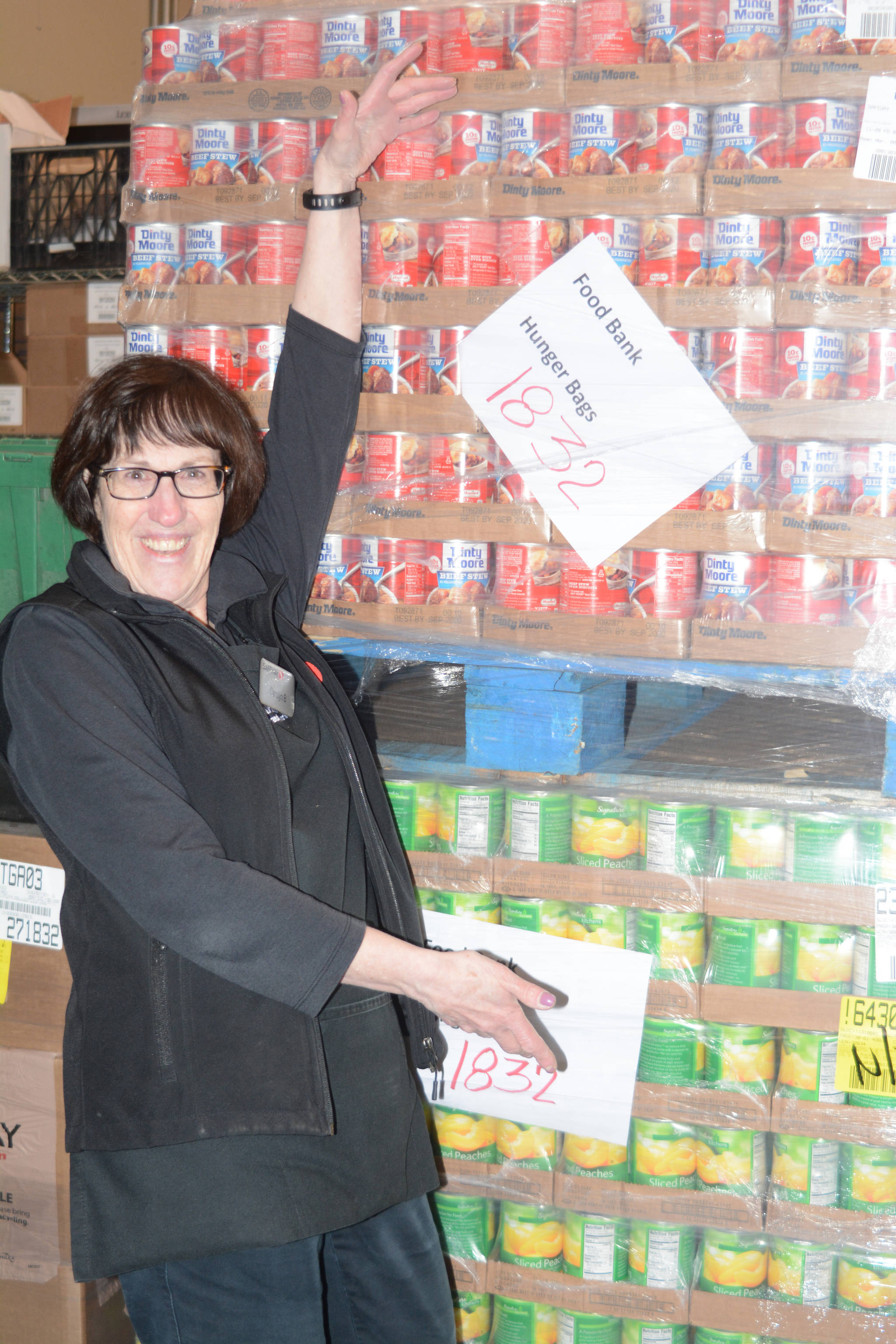 Homer Safeway checker Carolyn Bishop poses by a pallet of Hunger Bag food on Tuesday, Dec. 5, 2017. Bishop was one of the top checkers at the store who sold the Hunger Bags to customers as part of Safeway’s Hunger Bag project. Store Manager Bob Malone said about 1,300 bags at $10 each had been sold at the Homer store since Nov. 1. Through a national program, Safeway sells the bags and donates food to charities chosen by local stores. Pallets of food are organized at the Anchorage warehouse and sent to Homer. This year’s Homer Hunger Bags went to the Homer Community Food Pantry. Crew from the U.S. Coast Guard Cutter Naushon helped deliver food from Safeway to the food pantry. “This year, from what I understand, the need is more than normal,” Malone said. (Photo by Michael Armstrong, Homer News)