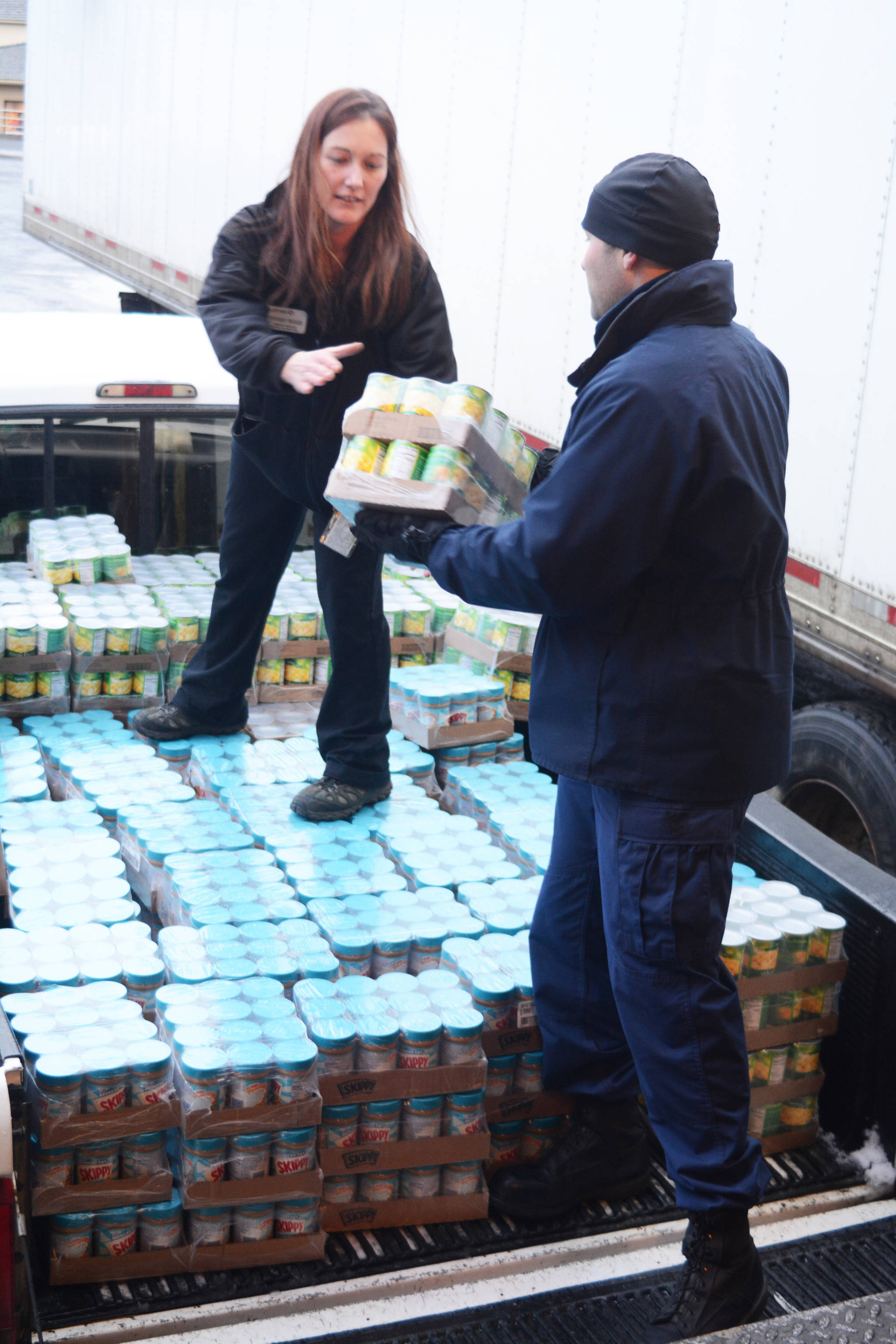 U.S. Coast Guard Cutter Naushon crew member James Bannon, right, helps Homer Safeway assistant store manager Tiffany Biggs, center, load Hunger Bag food onto a truck, Dec. 5, 2017. Bannon and fellow crew member Jordan Dorchin delivered food to the Homer Community Food Pantry on Tuesday that had been purchased by Safeway customers as part of its Hunger Bag project. Store Manager Bob Malone said about 1,300 bags at $10 each had been sold at the Homer store since Nov. 1. Through a national program, Safeway sells the bags and donates food to charities chosen by local stores. Pallets of food are organized at the Anchorage warehouse and sent to Homer. “This year, from what I understand, the need is more than normal,” Malone said. (Photo by Michael Armstrong, Homer News)