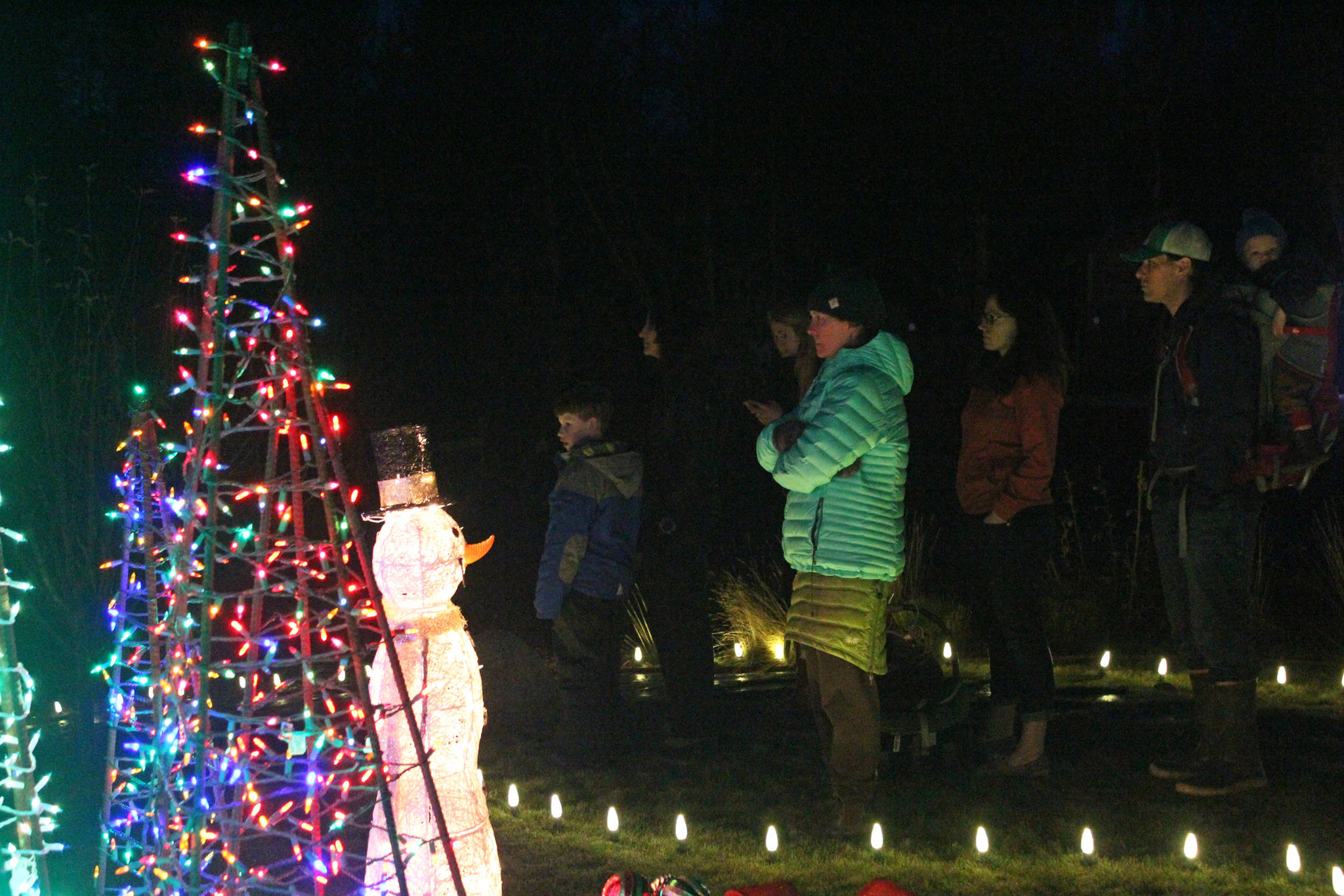 A small crowd of people pauses to watch the Homer High School Swing Choir perform Saturday, Dec. 16, 2017 at the Bear Creek Winery Garden of Lights near Homer, Alaska. (Photo by Megan Pacer/Homer News)