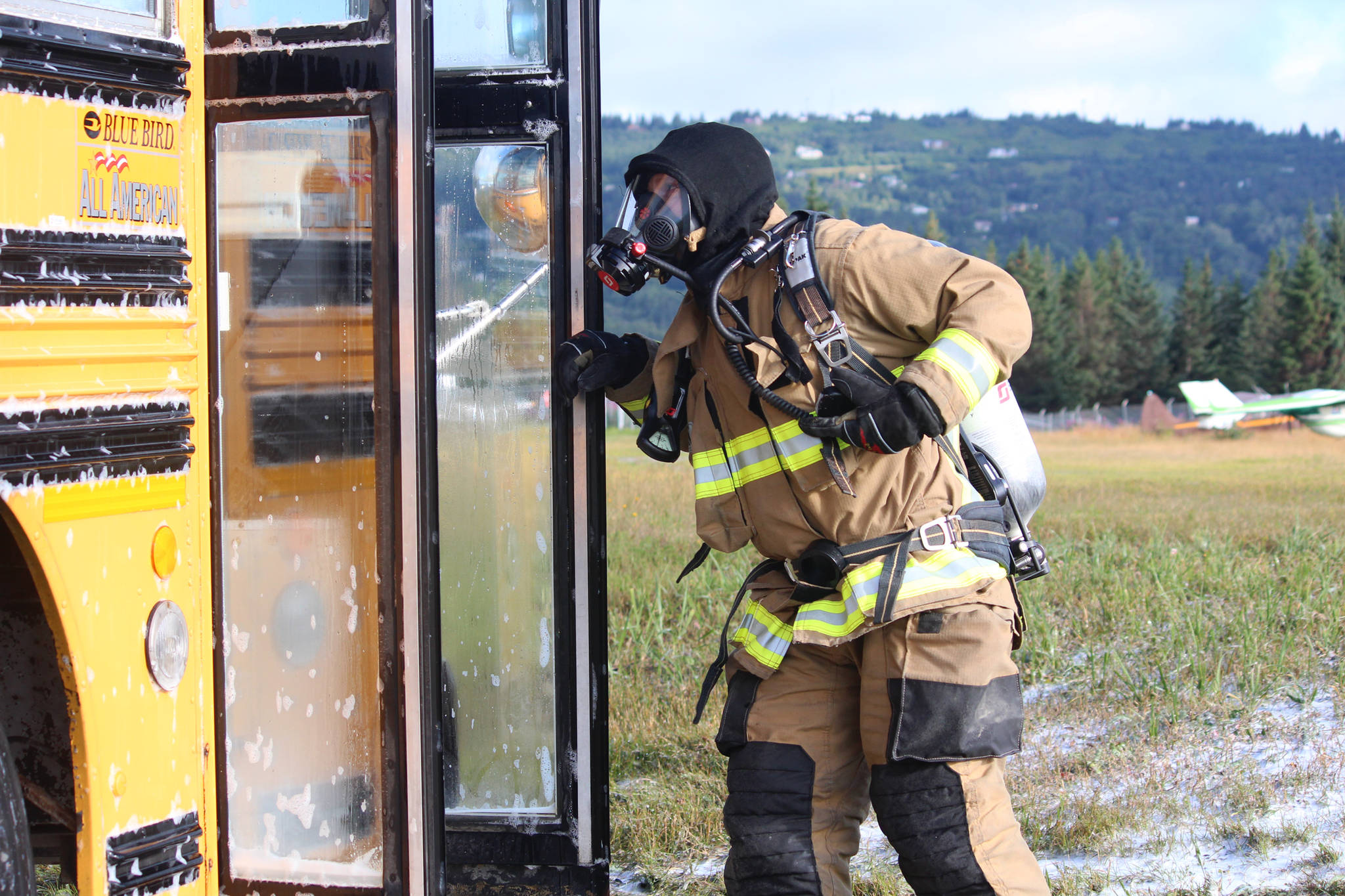 Firefighter Jesse Sherwood peers into a bus after spraying it down with foam during a simulated plane crash exercise Saturday, Aug. 19, 2017 at the Homer Airport in Homer, Alaska. He and members of several area emergency response agencies, along with airport personnel, completed the drill with the help of more than 20 volunteer “victims.” The drill is required every three years for the airport to stay in Federal Aviation Administration compliance. (Photo by Megan Pacer/Homer News)