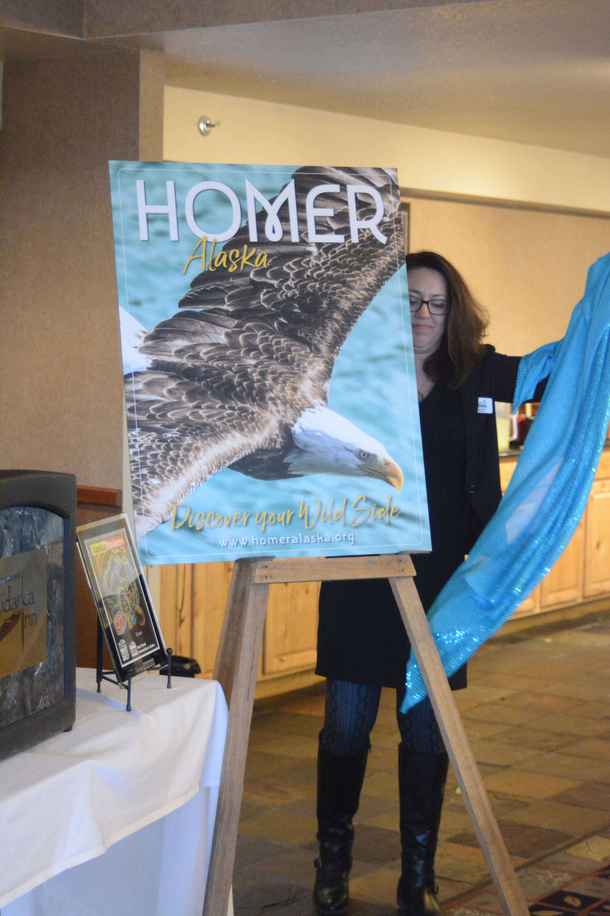 Homer Chamber of Commerce and Visitor Center board of director President Kari Ann Baker unveils the cover of the 2018 tourism and recreation guide at the chamber’s annual meeting on Tuesday, Jan. 16, 2018 at the Best Western Bidarka Inn in Homer, Alaska. The cover photo was taken by Collin Walker and picked in a contest held by the chamber. (Photo by Michael Armstrong, Homer News)