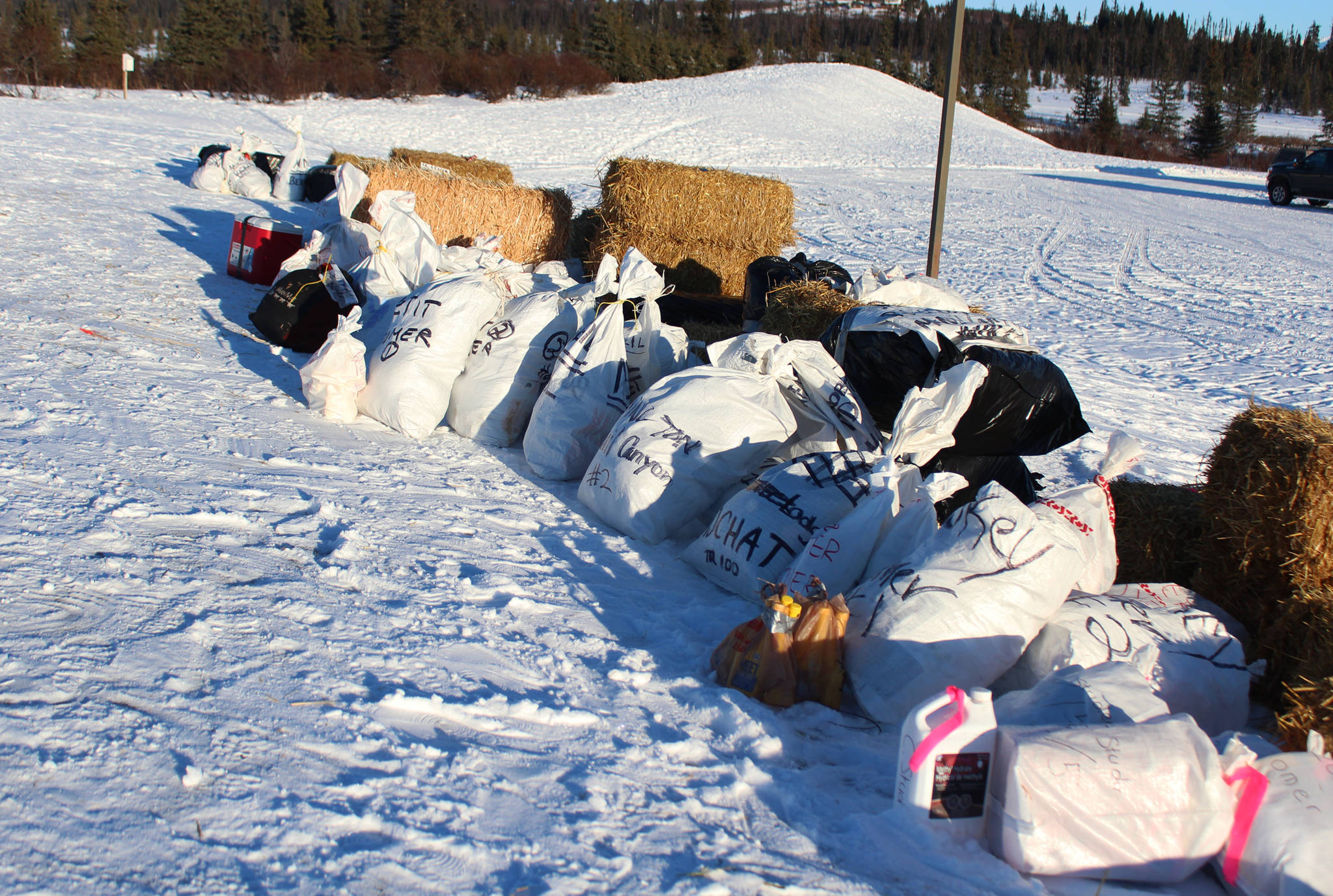 Bags of supplies and bales of hay await their corresponding mushing teams at a race checkpoint Saturday, Jan. 27, 2018 outside McNeil Canyon Elementary School near Homer, Alaska. (Photo by Megan Pacer/Homer News)