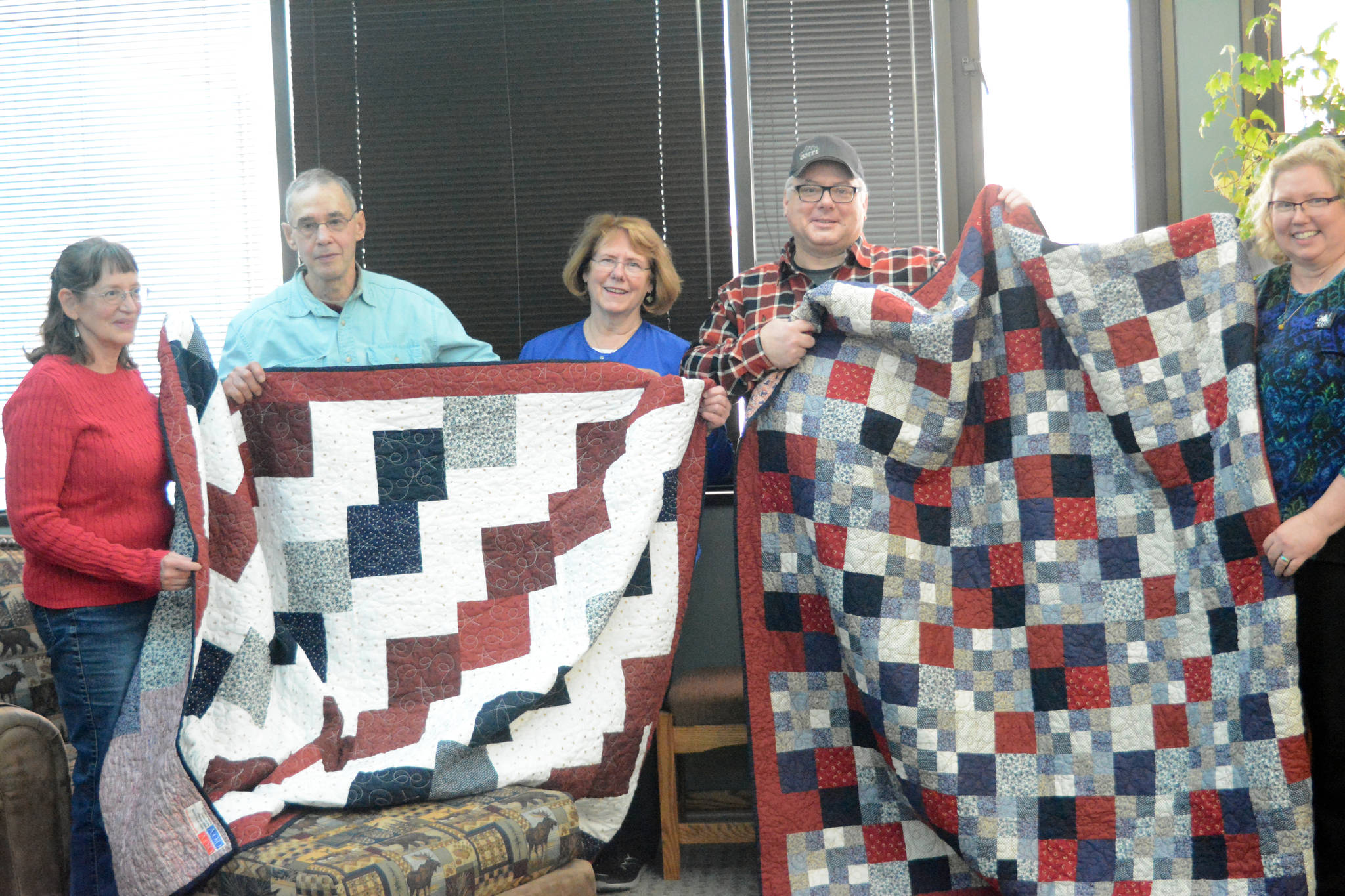 Jay Greene, second from left, and Andrew Hodnik, second from right, on Tuesday, Feb. 6, 2018, hold up Quilts of Valor given to them and made by Dana Moore, far left, and Connie Isenhour, far right. The quilts are a project of Faith Friday Friends, a group at Faith Lutheran Church. Under the national program volutneers make quilts to honor service members and veterans touched by war. Green flew 196 combat missions in Vietnam as a U.S. Navy pilot from 1967-68 and Hodnik served in the U.S. Army as a combat engineer from 1989-93, including tours in Operation Desert Storm and Somalia. In the middle is Hodnik’s mother, Dr. Vicky Hodnik. The quilts were presented at Hodnik’s dental office in Homer, Alaska. (Photo by Michael Armstrong, Homer News)