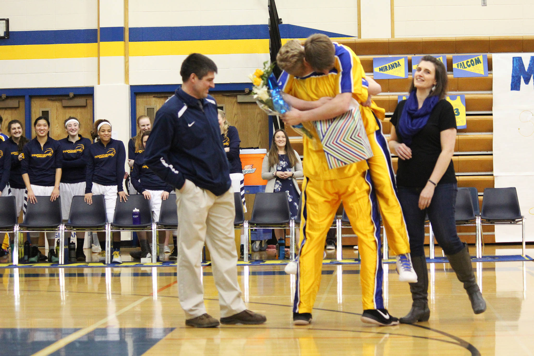 Homer’s Japheth McGhee picks up senior Joel Carroll in a big hug while presenting him with flowers and a gift during a Senior Night celebration before their basketball game against Seward High School on Friday, March 2, 2018 in Homer, Alaska. (Photo by Megan Pacer/Homer News)