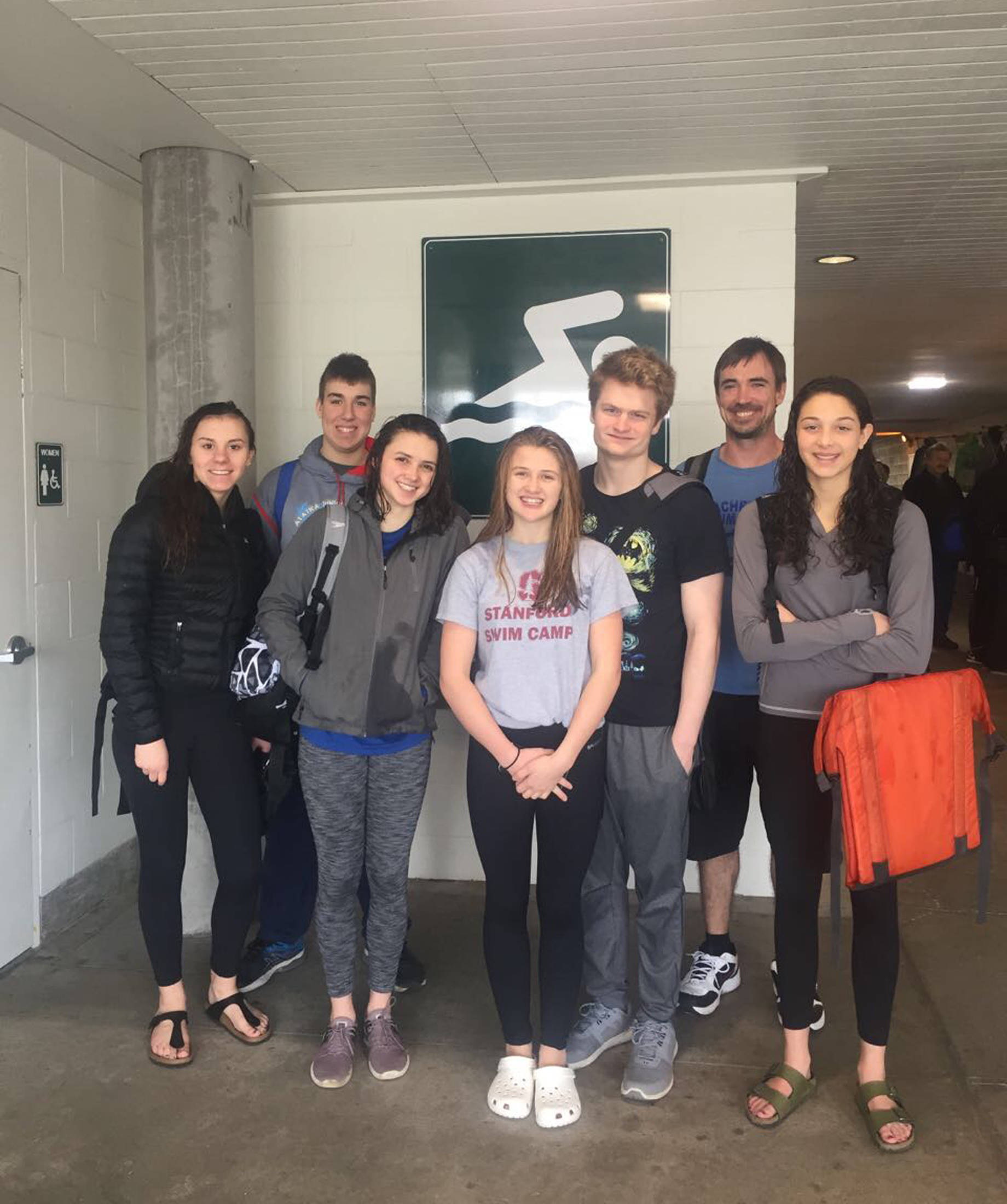 Photo by Britt Milne From left to right: Kira Milne, Jake Nelson, Ella Blanton-Yourkowski, Adeline Berry, Clayton Arndt, Coach Thad Gunther and Madison Story stand in front of the aquatic complex Beaverton, Oregon on Sunday, March 4.