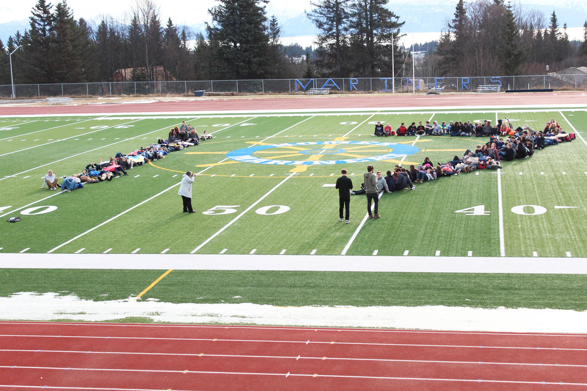 About 100 Homer High School students lie down on the school’s football field to form the number 17 on Wednesday, Feb. 21, 2018, to honor the students who were killed in the Feb. 14 mass shooting in Parkland, Florida. The Homer students staged a walkout at noon to advocate for safer schools. (Photo by Megan Pacer/Homer News)