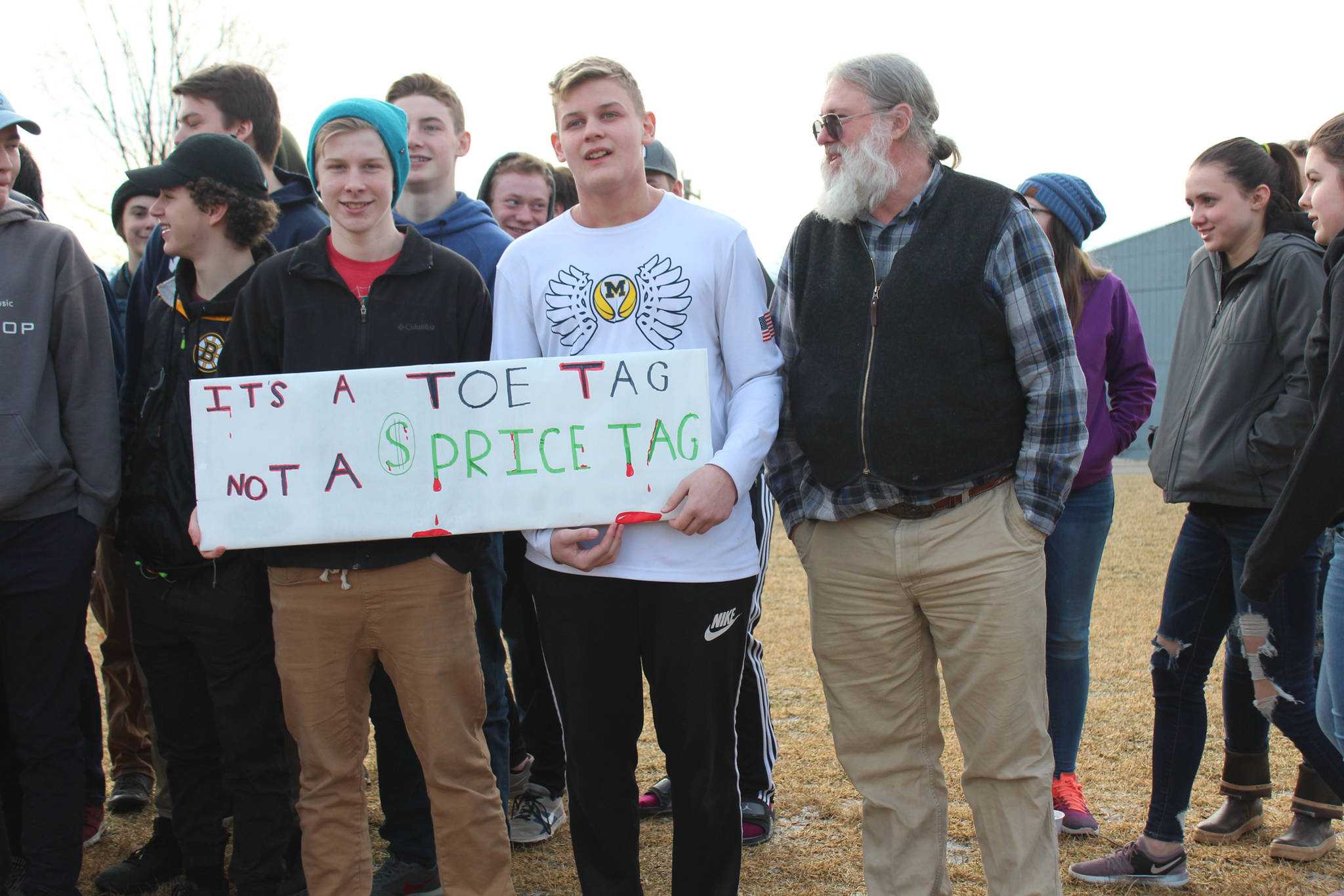 From left to right: Freshman Jack Strydom, freshman River Mann and science teacher Bruce Rife stand with a group of about 100 students and some staff who staged a walkout at Homer High School on Wednesday, Feb. 21, 2018 in Homer, Alaska. Their sign reads, “It’s a toe tag, not a price tag.” (Photo by Megan Pacer/Homer News)
