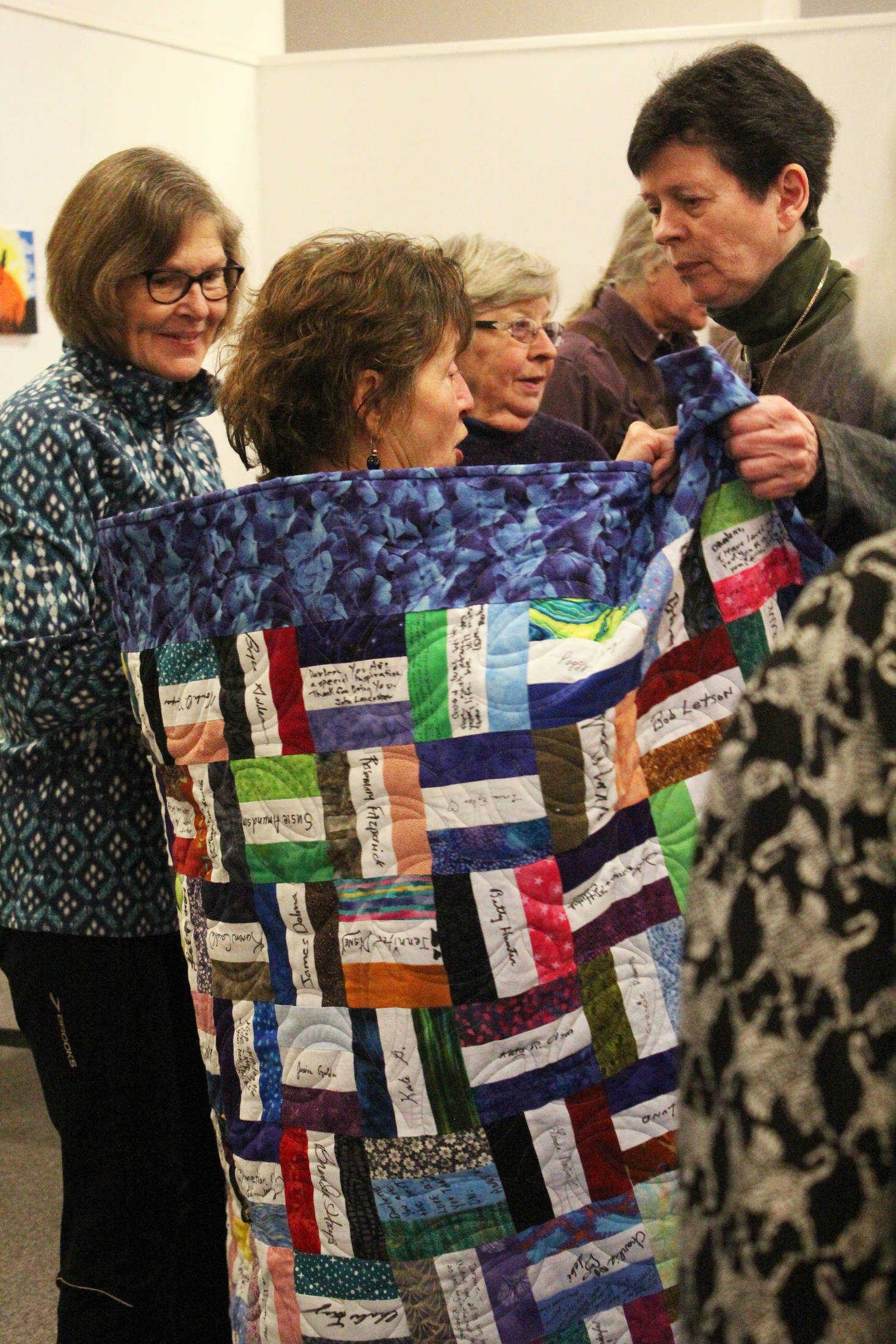 Darlene Hilderbrand wraps up in the quilt made to honor her retirement by Jane Regan, right, at a surprise party Sunday, March 18, 2018 at Homer Council on the Arts in Homer, Alaska. Hilderbrand worked at Hospice of Homer for 19 years. (Photo by Megan Pacer/Homer News)