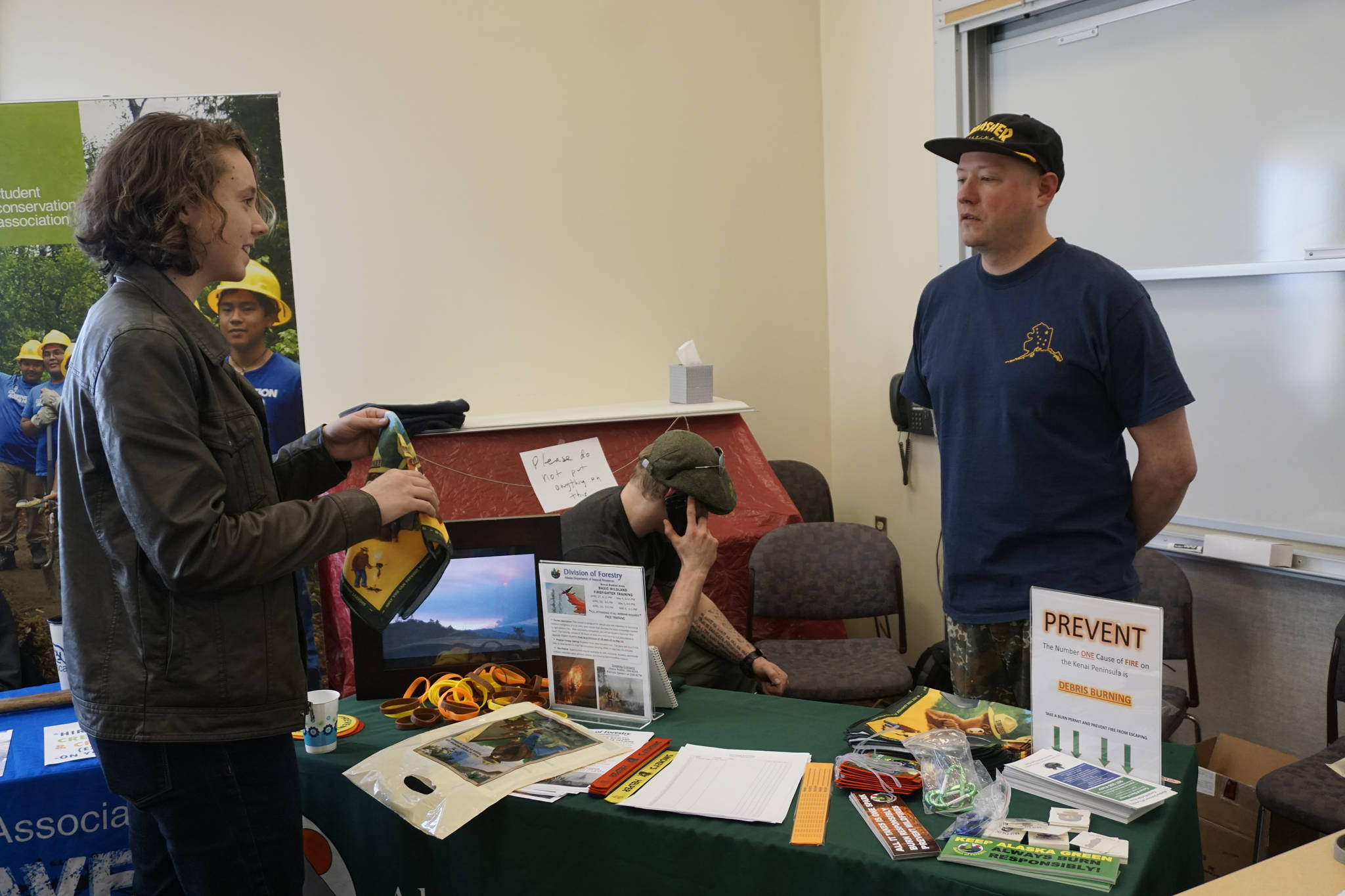 Homer High School student Ellie Syth, left, visits with wildland firefighter Aaron Seaton at the Alaska Division of Forestry table during the Kachemak Bay Campus College and Career Fair last Friday, March 30, 2018 in Homer, Alaska. About 400 students from 11 area schools as well as community members visited the annual event, said Kim Frost, KBC student and enrollment services coordinator. (Photo by Michael Armstrong/Homer News)
