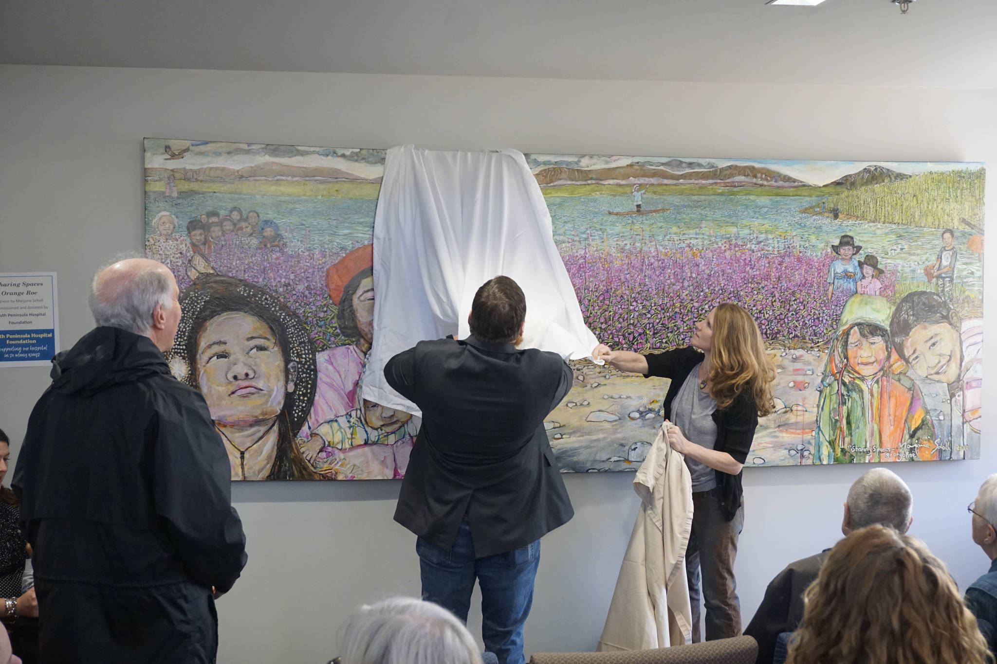 Homer artist Marjorie Scholl, far right, unveils her new painting, “Sharing Spaces Orange Roe,” at an open house for the expanded and remodeled clinic last Friday, March 30, 2018 on Bartlett Street in Homer, Alaska. The South Peninsula Hospital Foundation commissioned and donated the painting to the clinic. (Photo by Michael Armstrong, Homer News)