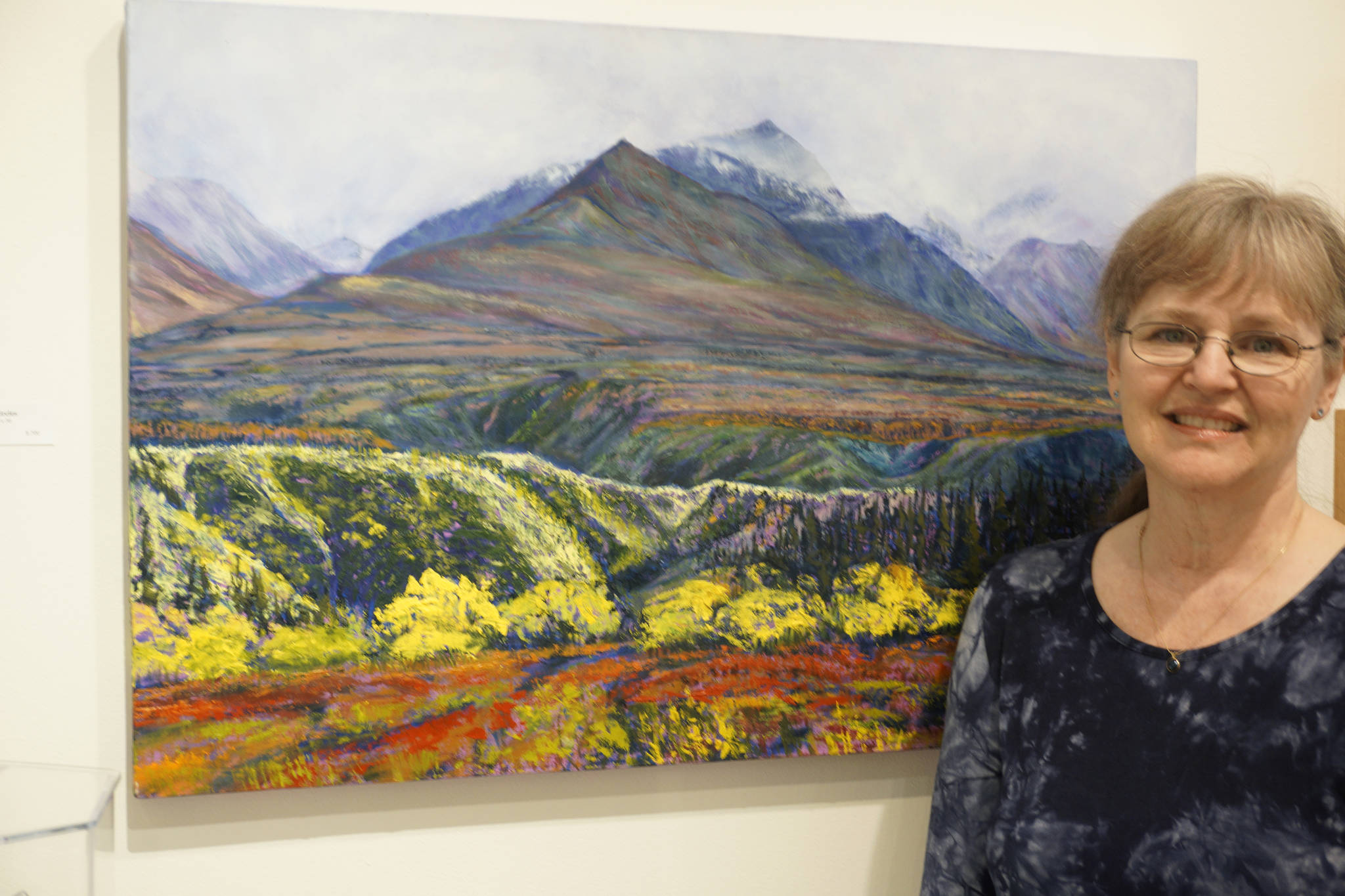 The long view Homer artist Rita Pfenninger poses last Friday for the opening of her show, Mountain, Foliage, Ocean, Sky at Fireweed Gallery. The painting shows the Chugach Mountains as seen from Sheep Mountain Lodge, Glenn Highway. Also in the show is jewelry by her husband, Larry Hoare.
