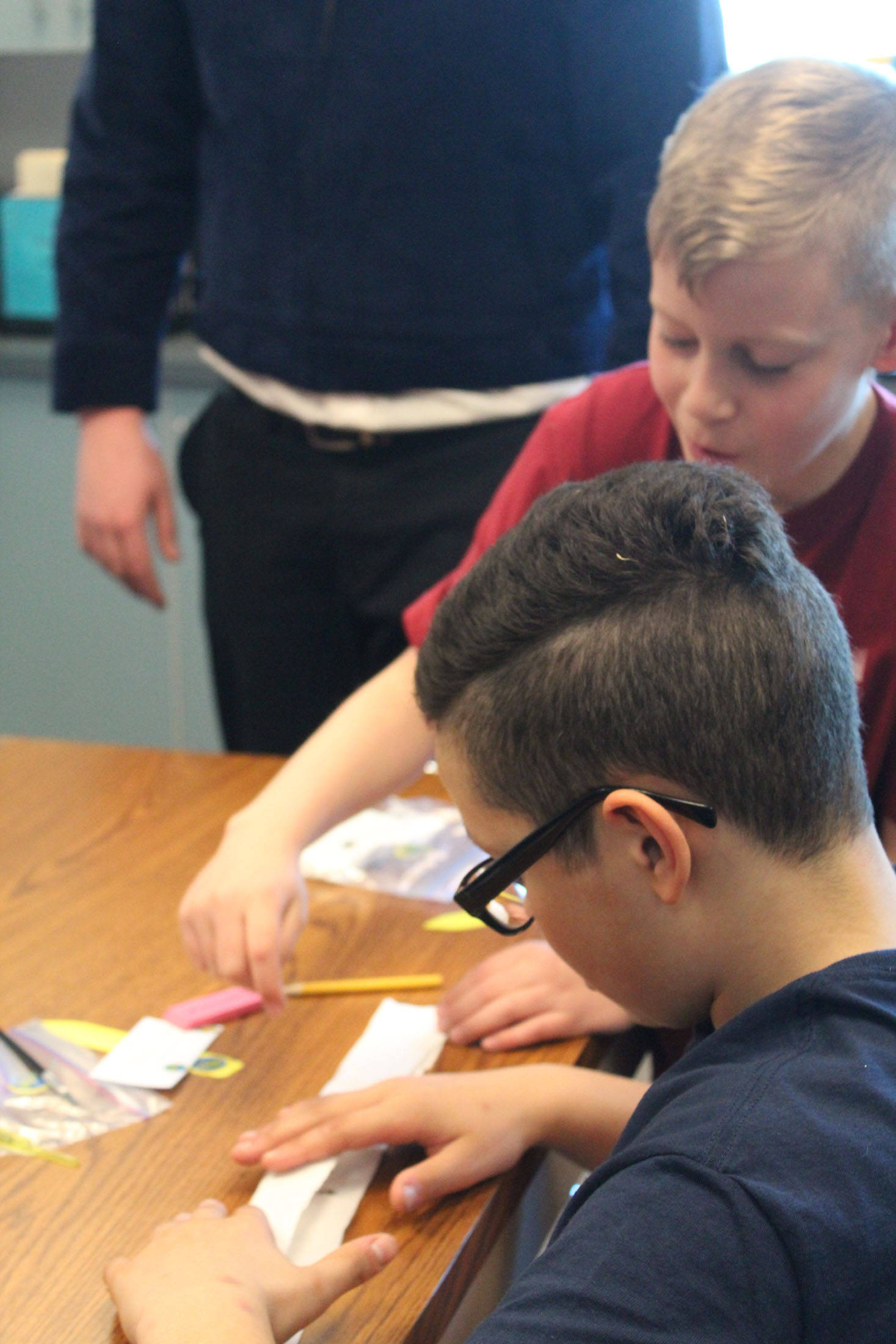 Fourth grader Kannon Hughes, background, helps sixth grader Ceiony Allen fold his seed tape, or a method of readying and storing seeds for later planting, on Tuesday, May 1, 2018 at Ninilchik School in Ninilchik, Alaska. Members of the Ninilchik chapter of the National FFA Organization visited the school to host educational sessions for Alaska Agriculture Day. (Photo by Megan Pacer/Homer News)