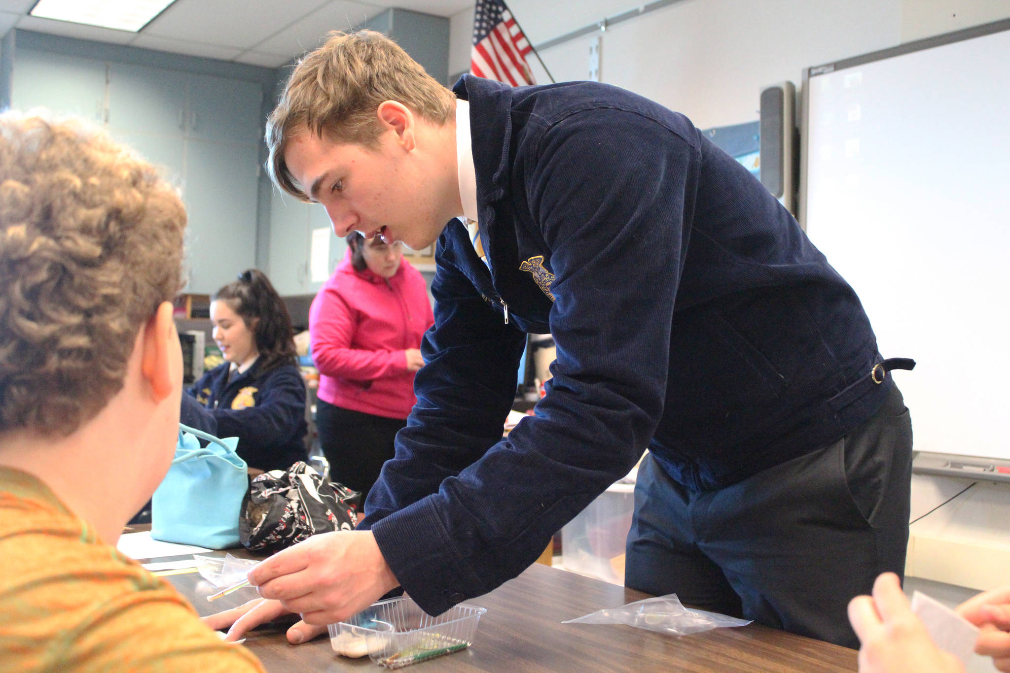 Ninilchik School senior Robert McGinnis shows younger students how to create a seed tape, or a way of storing vegetable seeds for later planting, on Tuesday, May 1, 2018 at the school in Ninilchik, Alaska. He and other representatives of Ninilchik’s chapter of the National FFA Organization visited the school for the first time to host educational sessions on Alaska Agriculture Day. (Photo by Megan Pacer/Homer News)