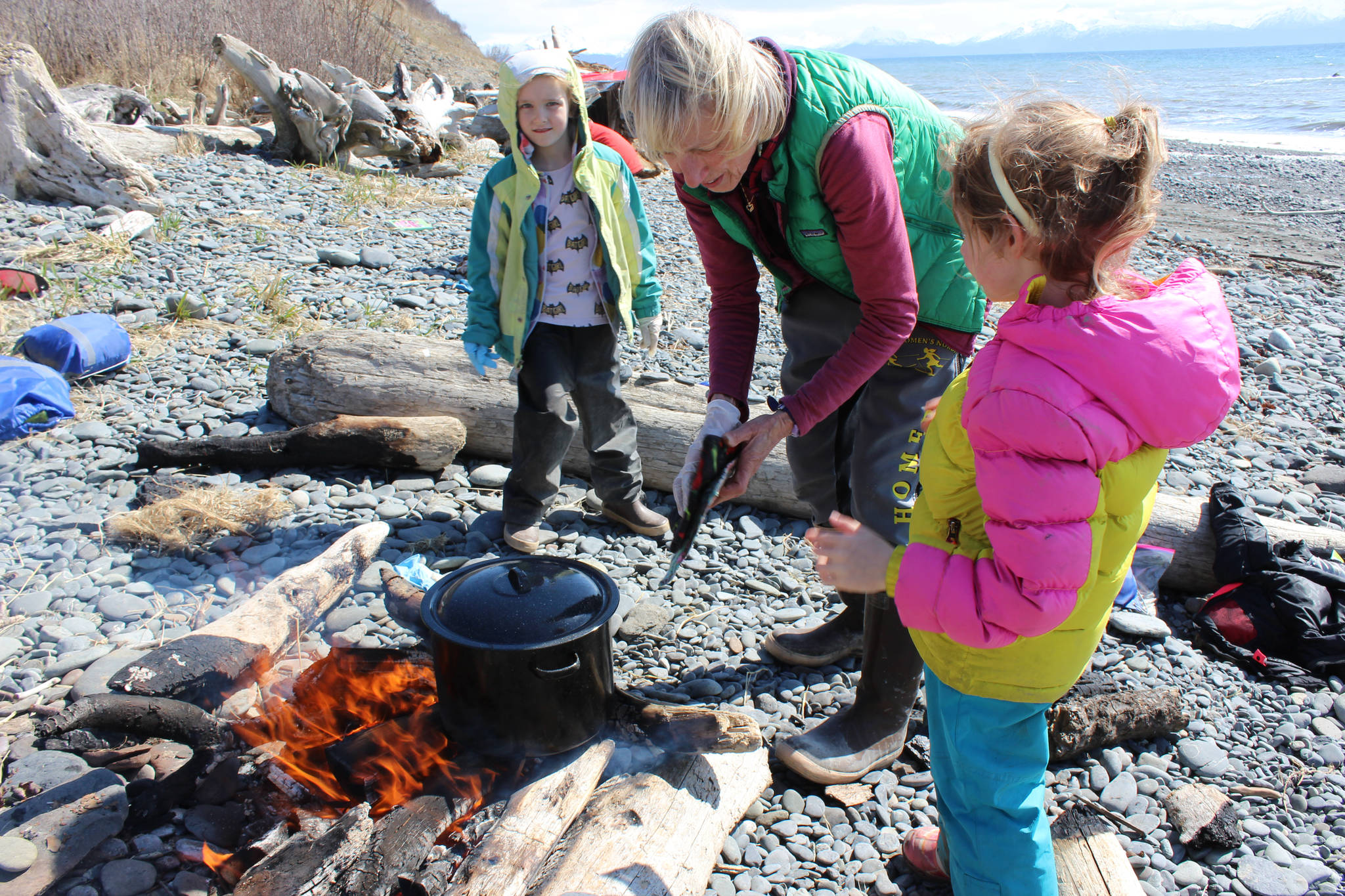 A May 2 outing for students in the Kenai Peninsula School District’s Wilderness Explorers program in Homer is an opportunity for volunteer Tania Spurkland (center) to teach Estelle Velsko (left) and Allie Barker (right) how to prepare stinging nettles over a campfire. (Photo by McKibben Jackinsky)