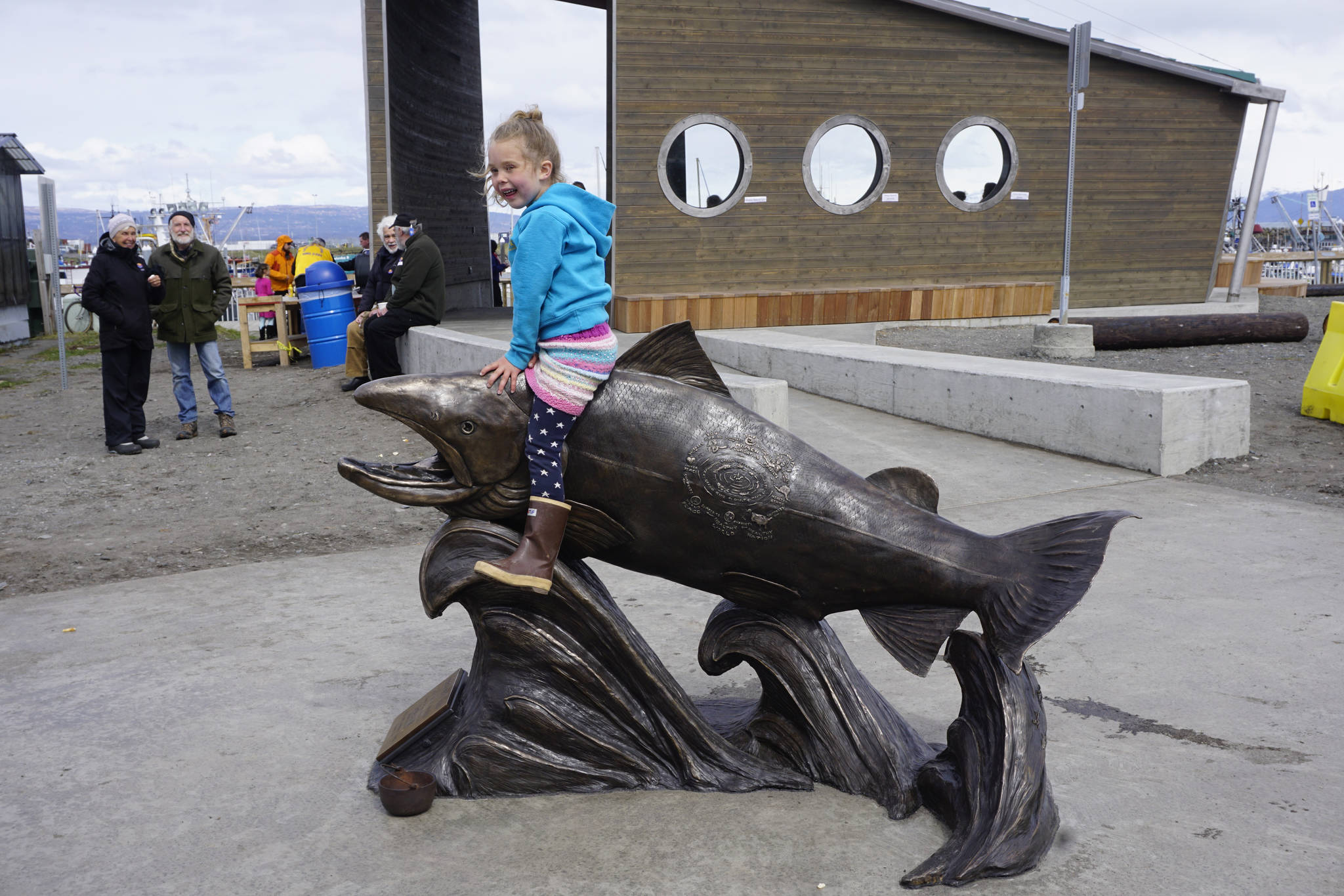 Isla Brown, age 5, sits on Wildheart, the Giving Salmon, sculpture Saturday, May 12, 2018 at the ribbon cutting for the Homer Boat House. (Photo by Michael Armstrong/Homer News)