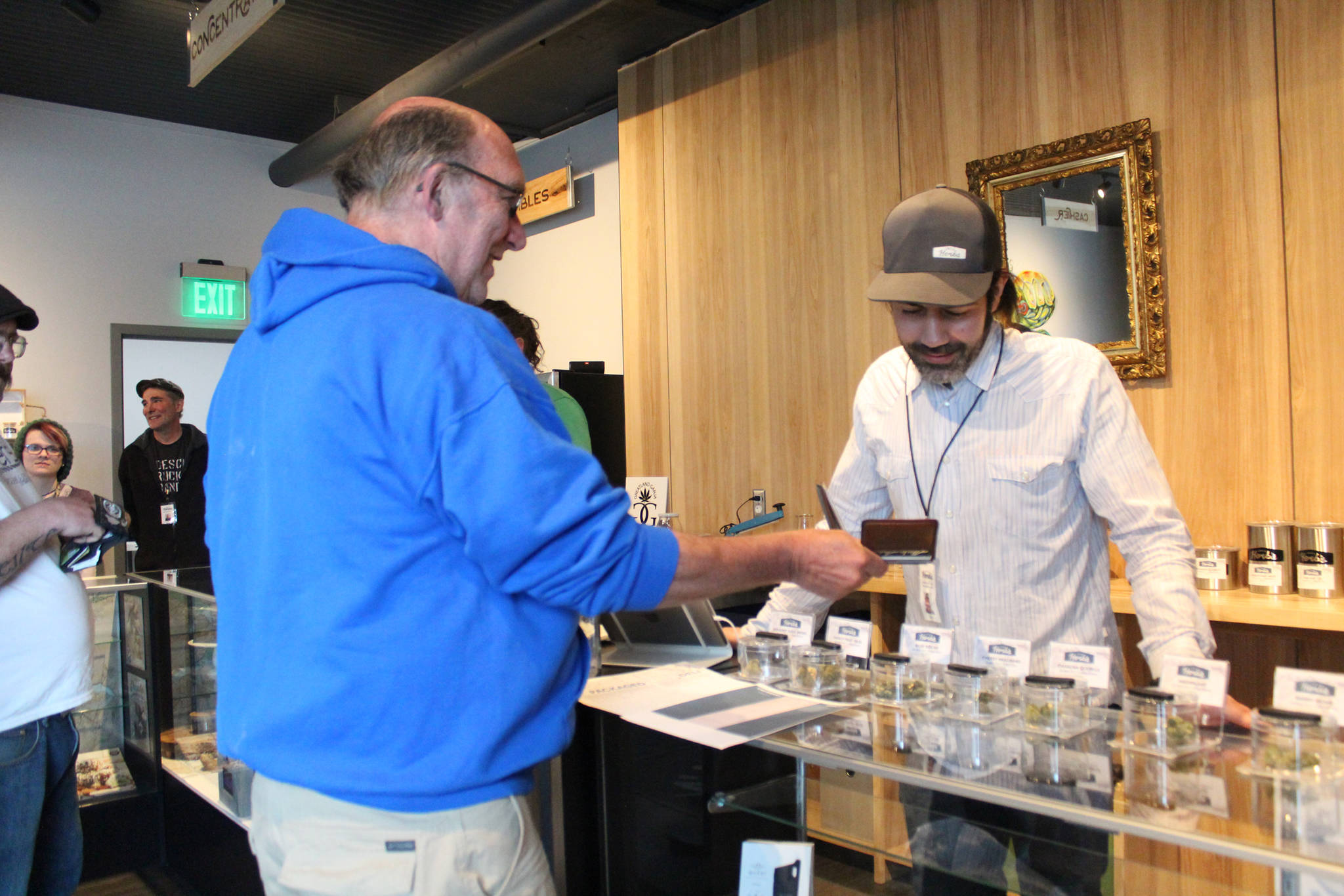 Photo by Megan Pacer/Homer News Former Homer City Council member David Lewis shows his ID to Aaron Stiassny on the opening day of Homer’s first marijuana retail store, Uncle Herb’s, on Thursday, May 24 in Homer. Stiassny will oversee the business for his father, Lloyd, who owns another branch in Anchorage.